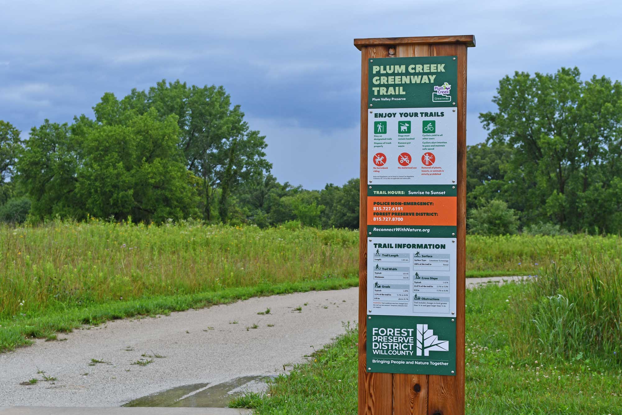 Trail sign with a limestone trail, vegetation, and trees in the background.