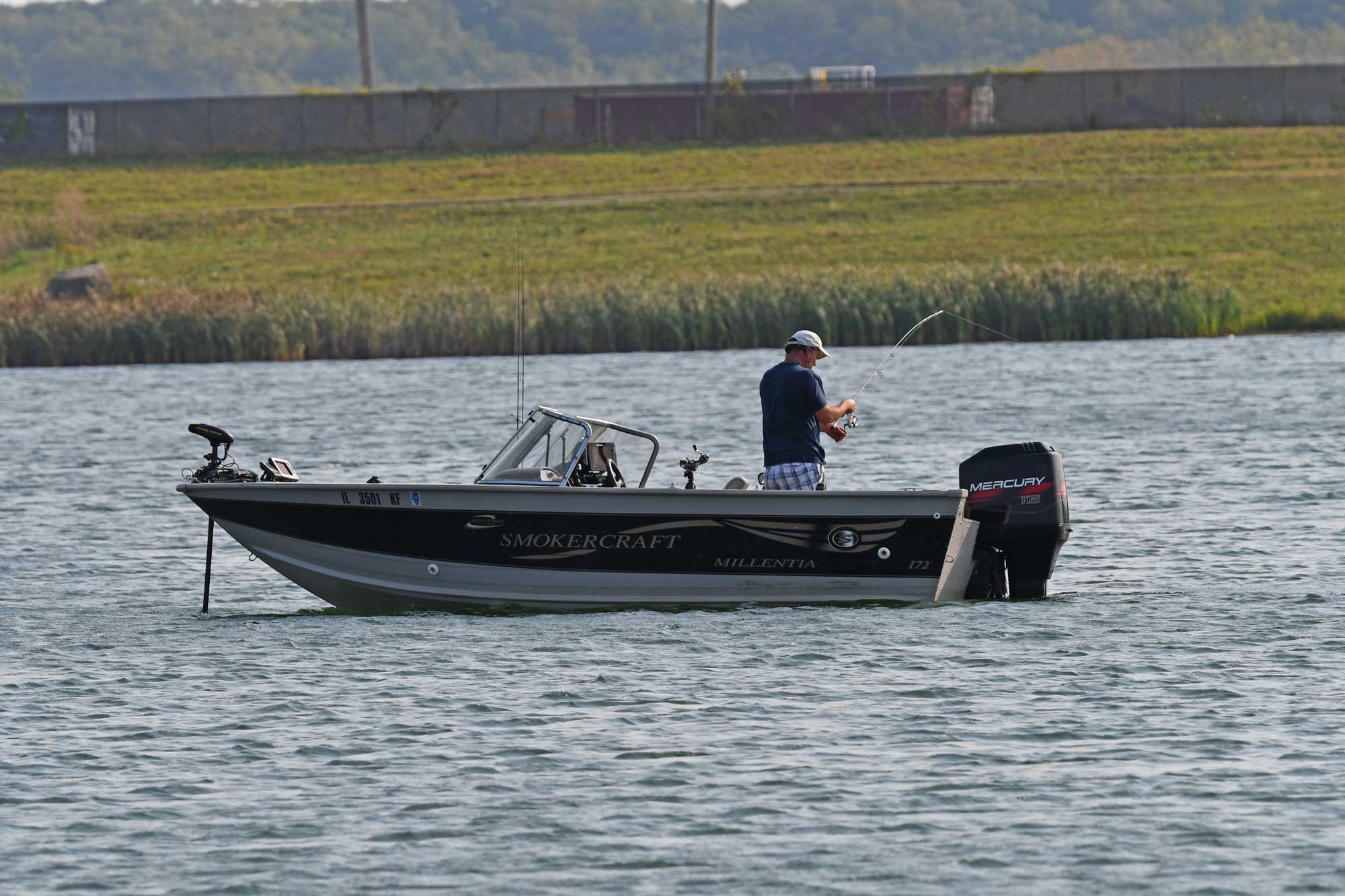 Person standing up in a boat while fishing with grasses in the background.