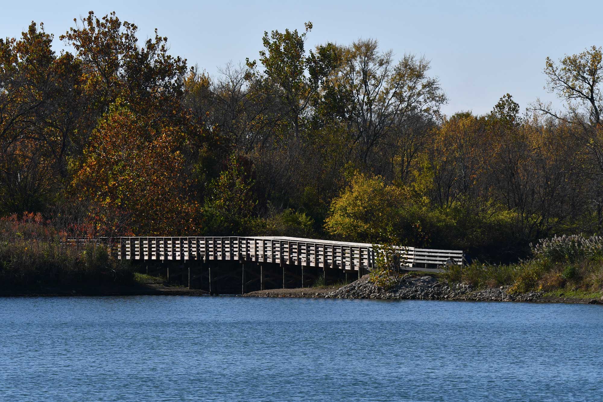A wooden bridge spanning a lake with trees in the background.