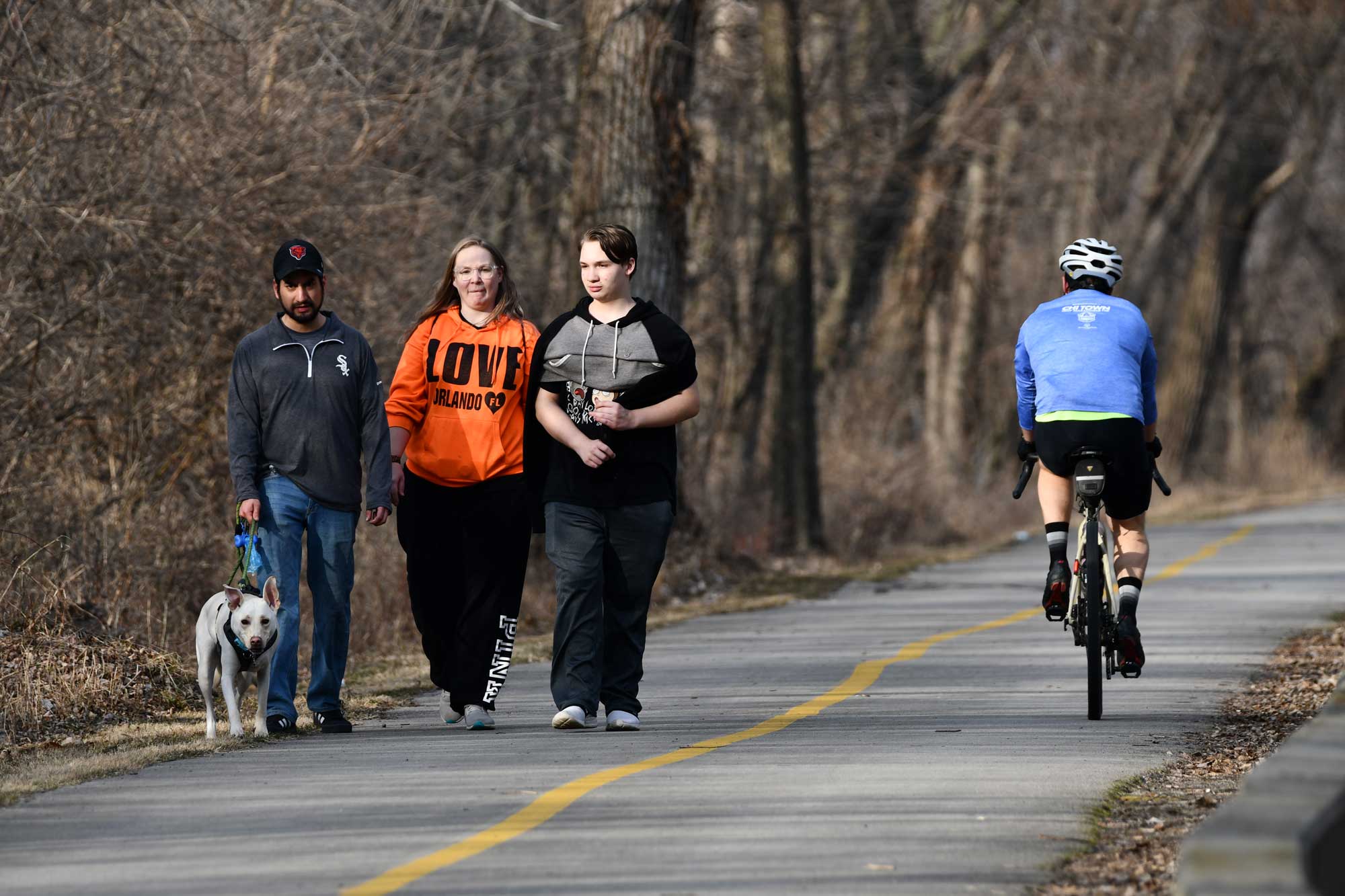People walking on a paved trail with a biker passing by and trees in the background.