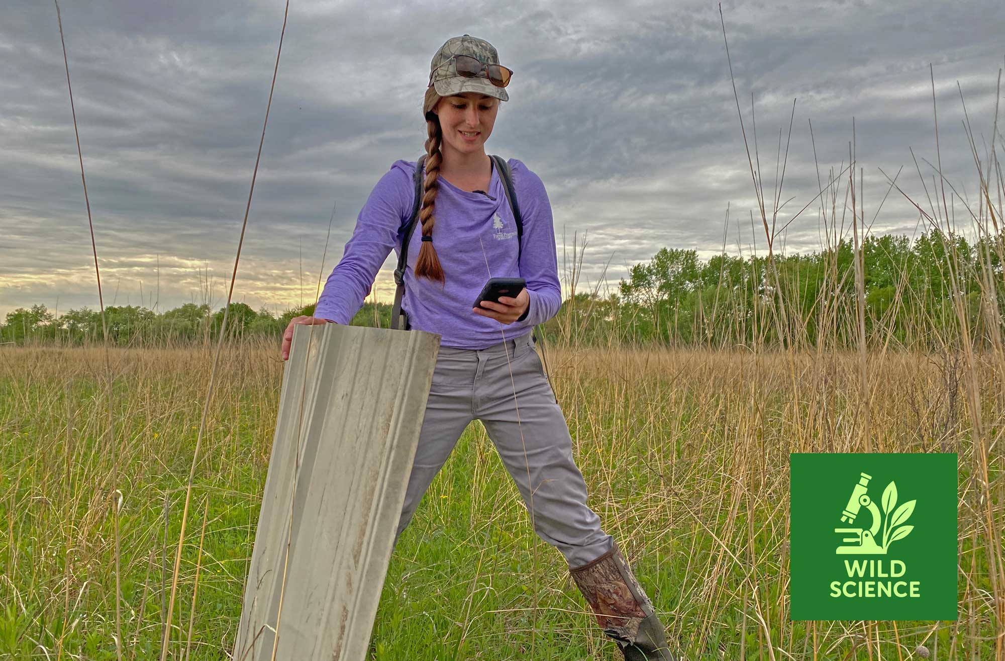 An ecologist stands in an open prairie while lifting a board.