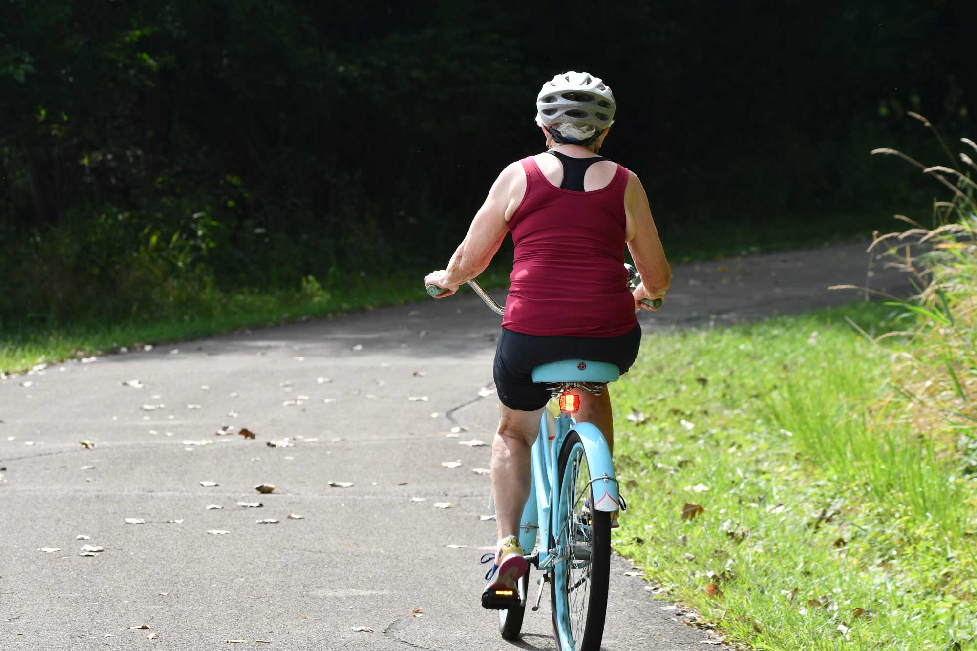 Person riding bike on a paved trail with vegetation in the background.