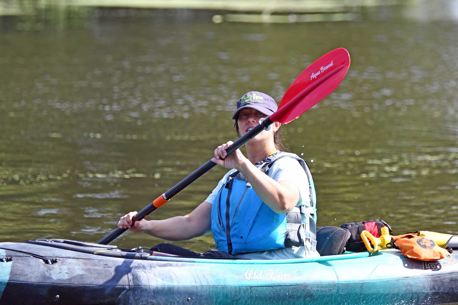 A person sitting in a light blue kayak in the water, holding up the paddle.