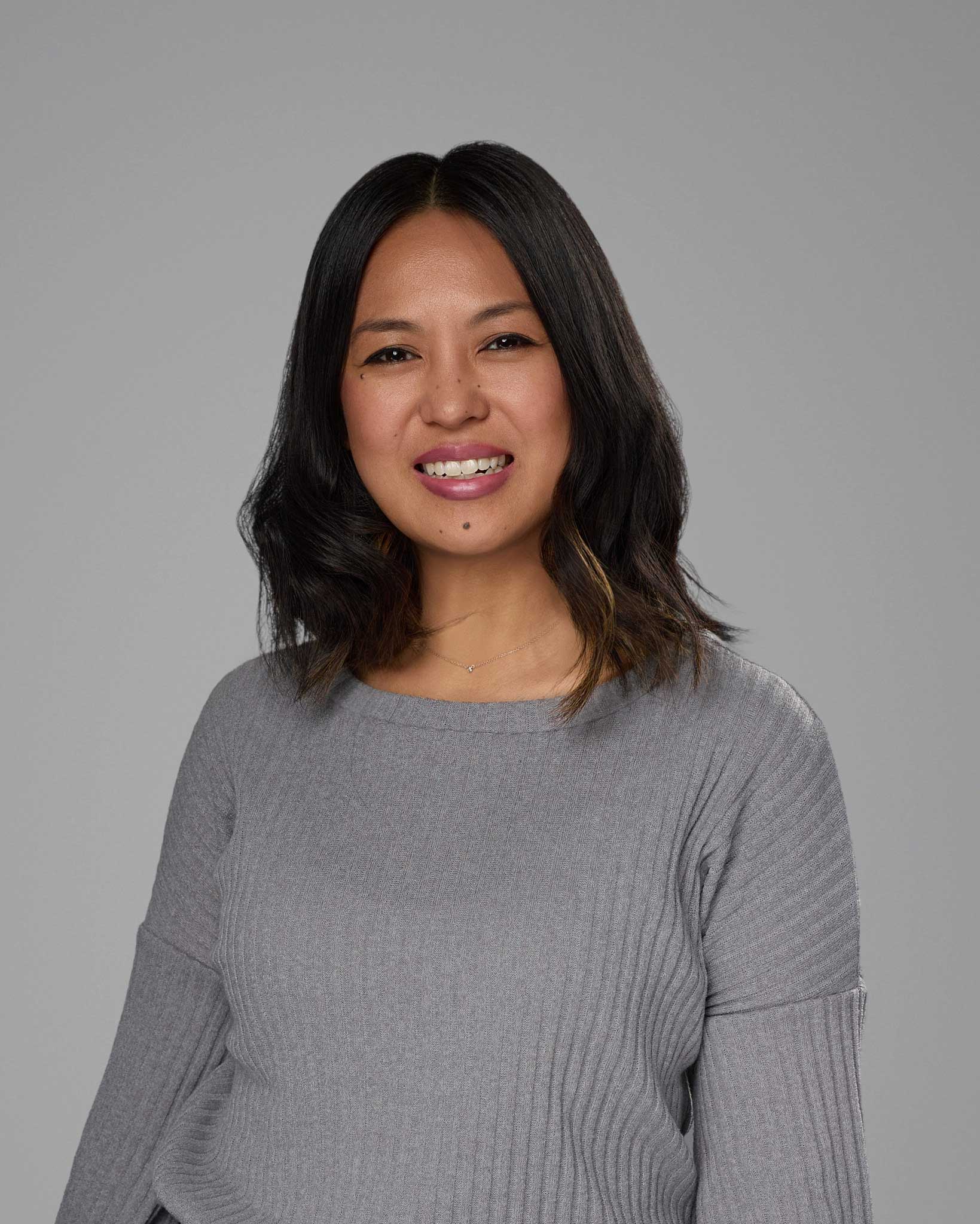 a woman with dark hair wearing a grey sweater