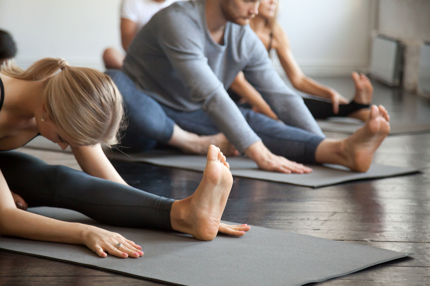 People lined up sitting on yoga mats with legs and arms stretched toward their feet.