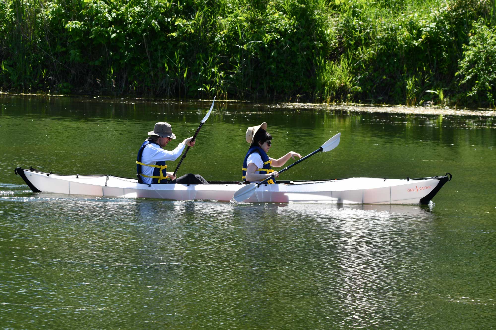 Two people in a canoe with water and tree line in the background.