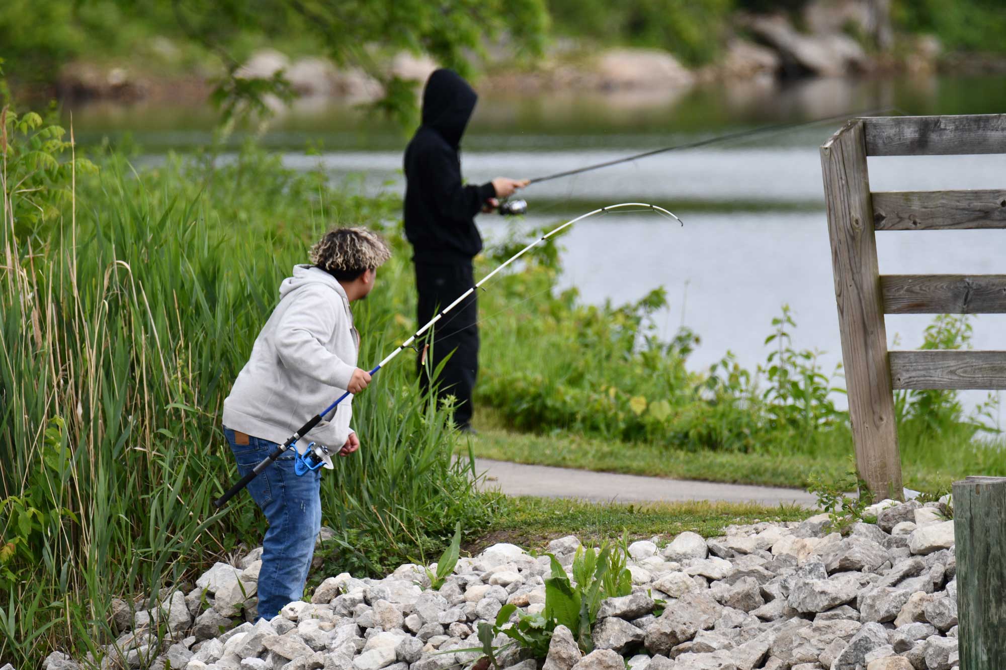People fishing with vegetation and water in the background.
