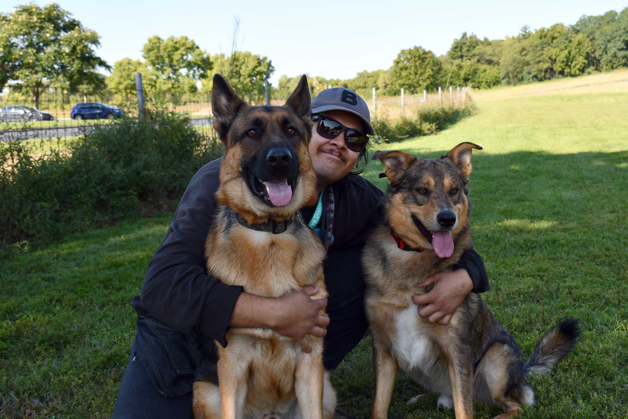 Person hugging two dogs in a dog park.