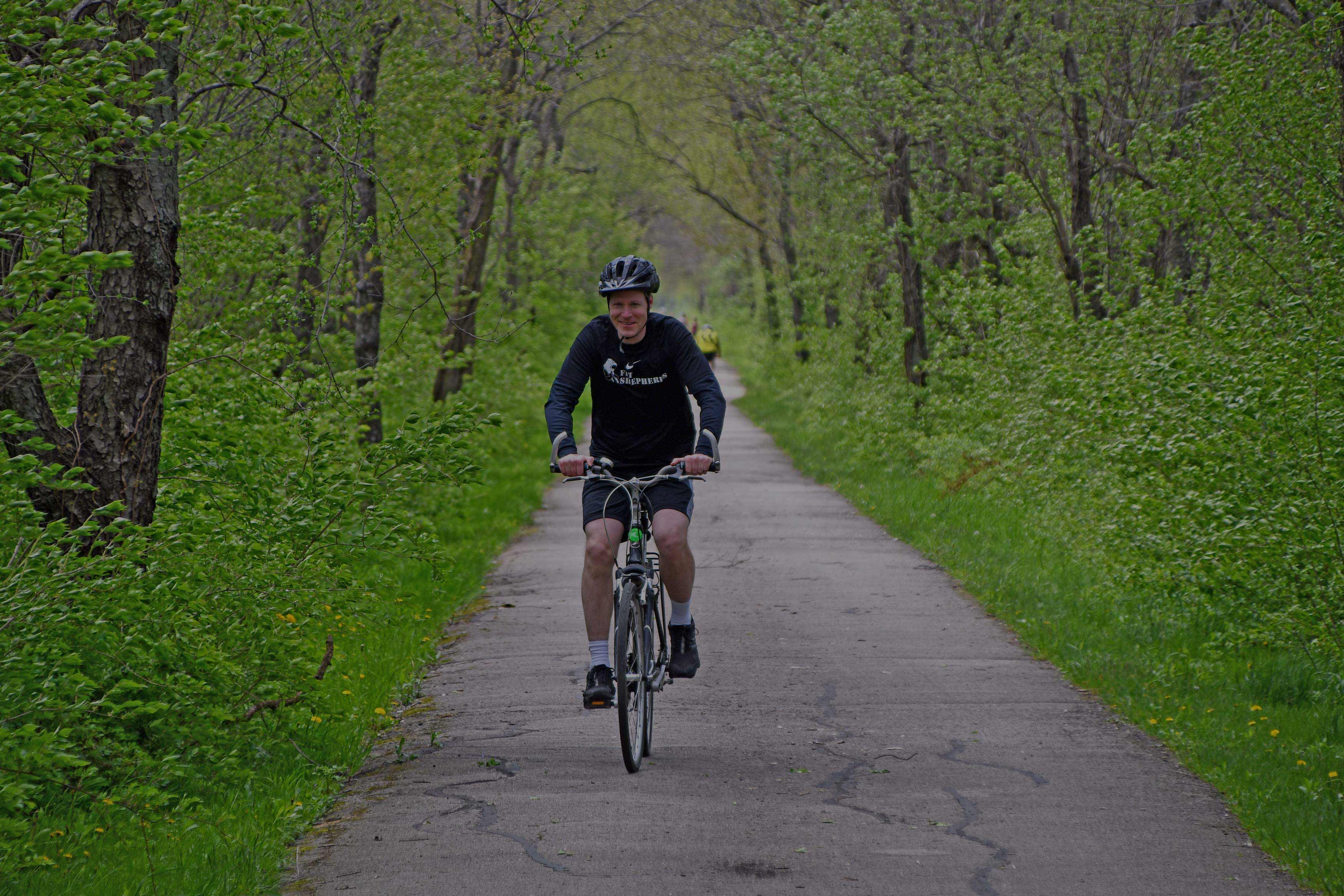 A cyclist rides on a tree-lined trail.