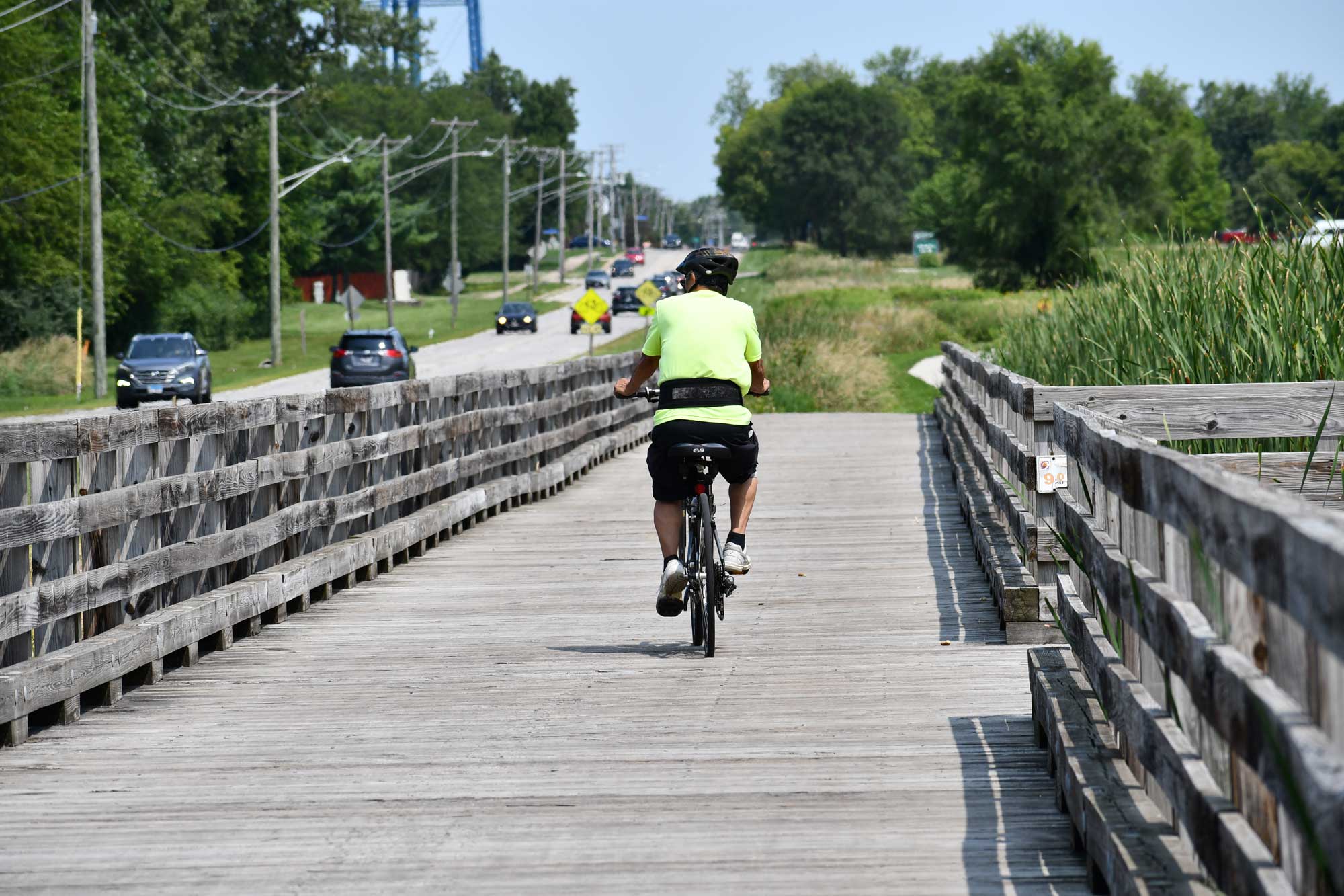 Person riding bike on wooden bridge with vegetation in the background.