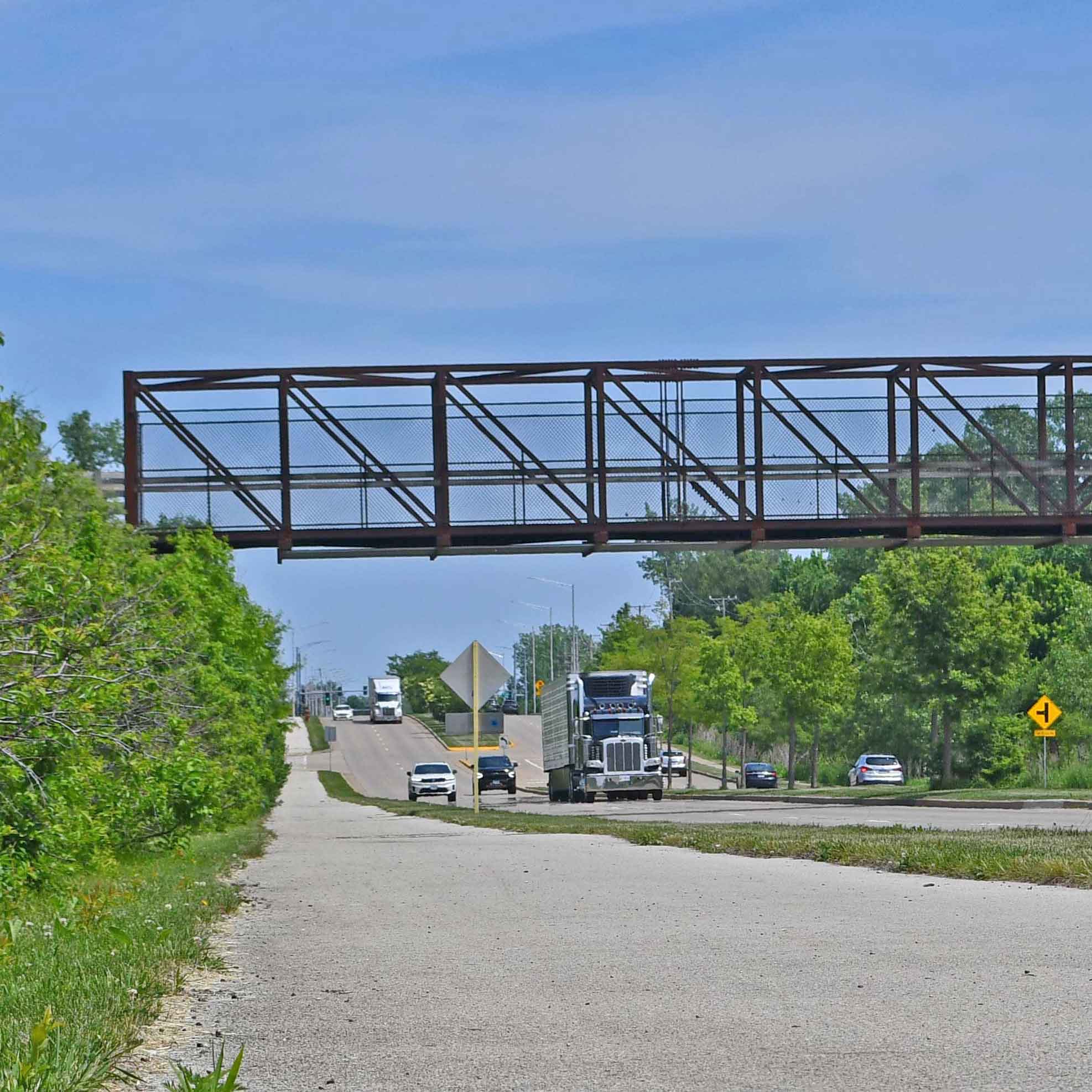 Trail running along a road with a bridge in background and vehicles in view.