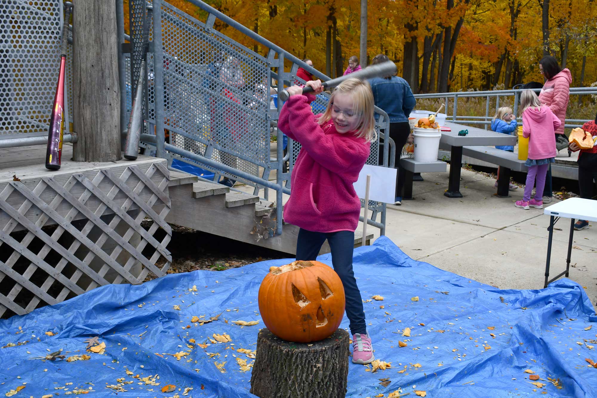 A child holding a bat over their head, preparing to smash a jack-o'-lantern. 