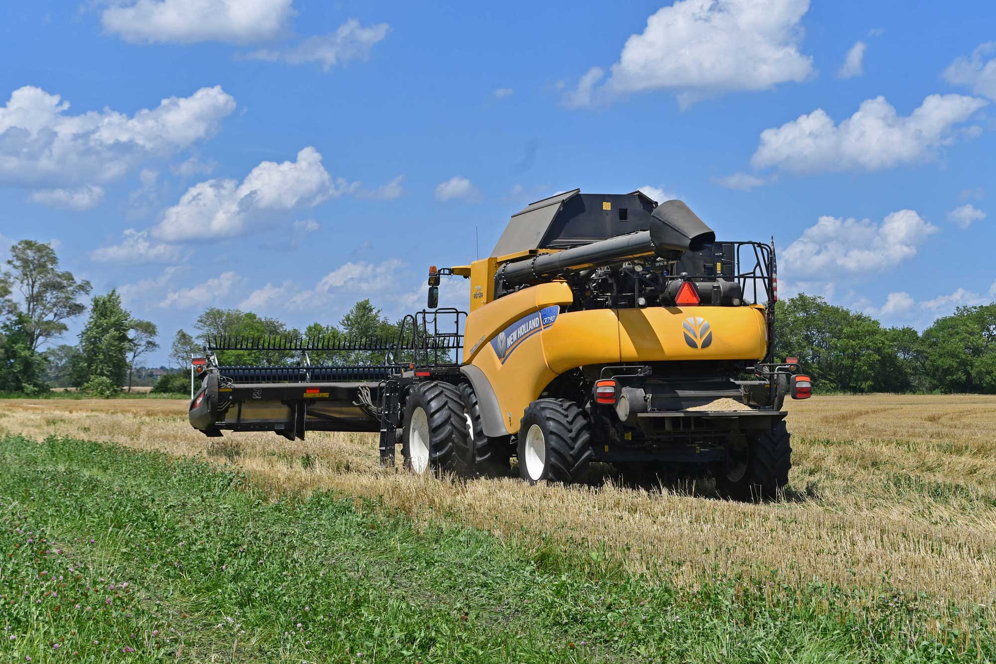 Combine driving through a wheat field with a partly cloudy sky in the background.