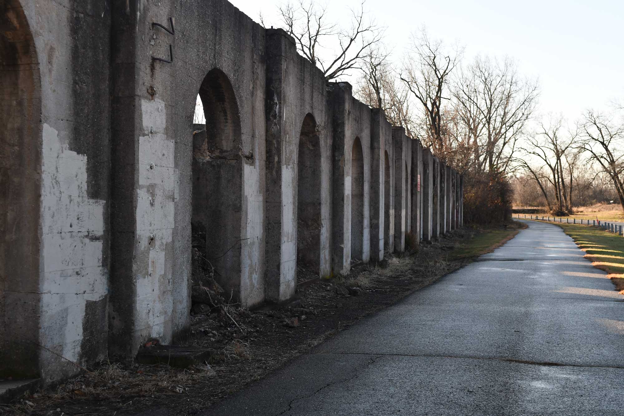 The ruins of a building full of concrete arches next to a paved trail. 