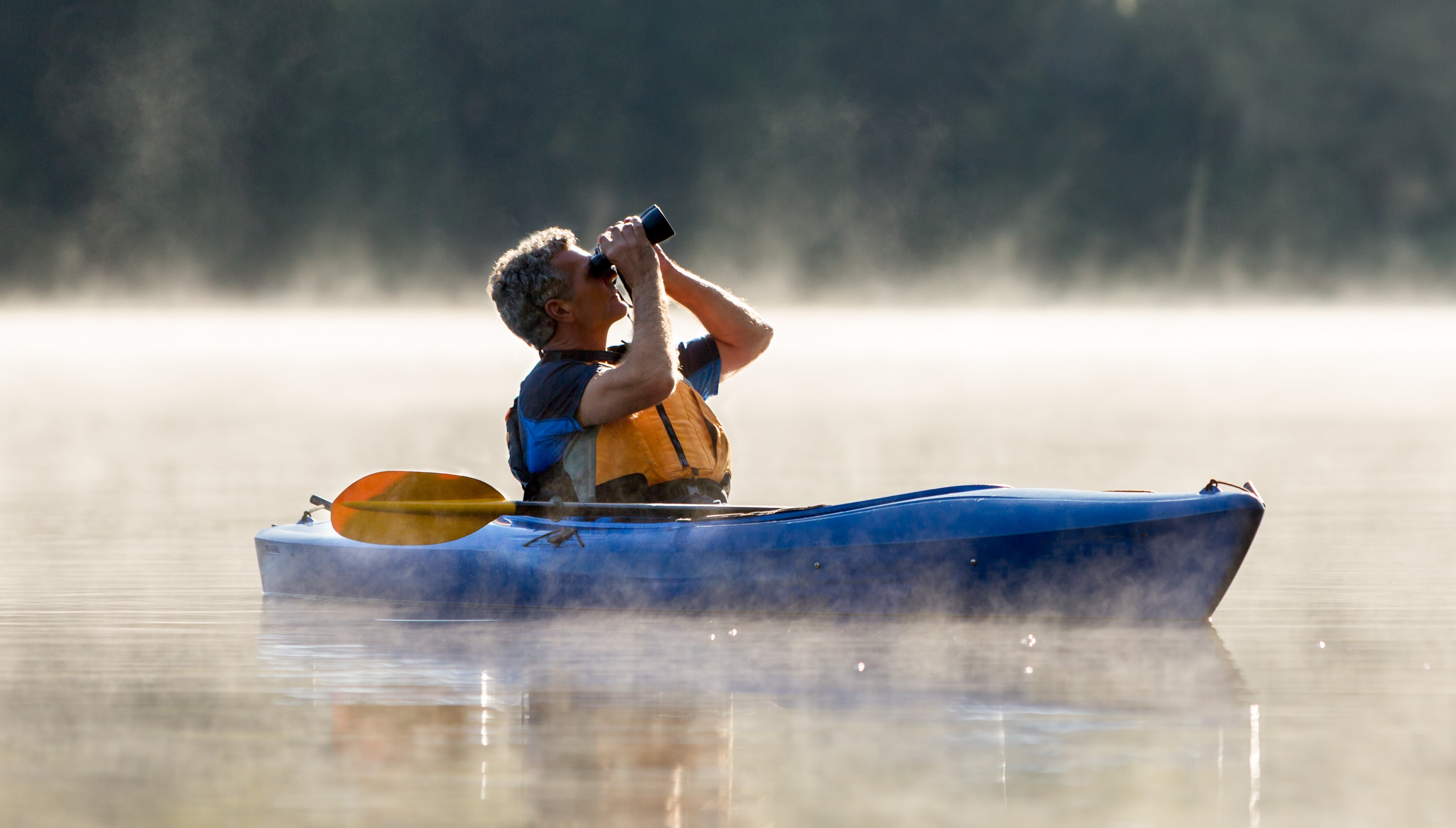 A kayaker looking out of binoculars.