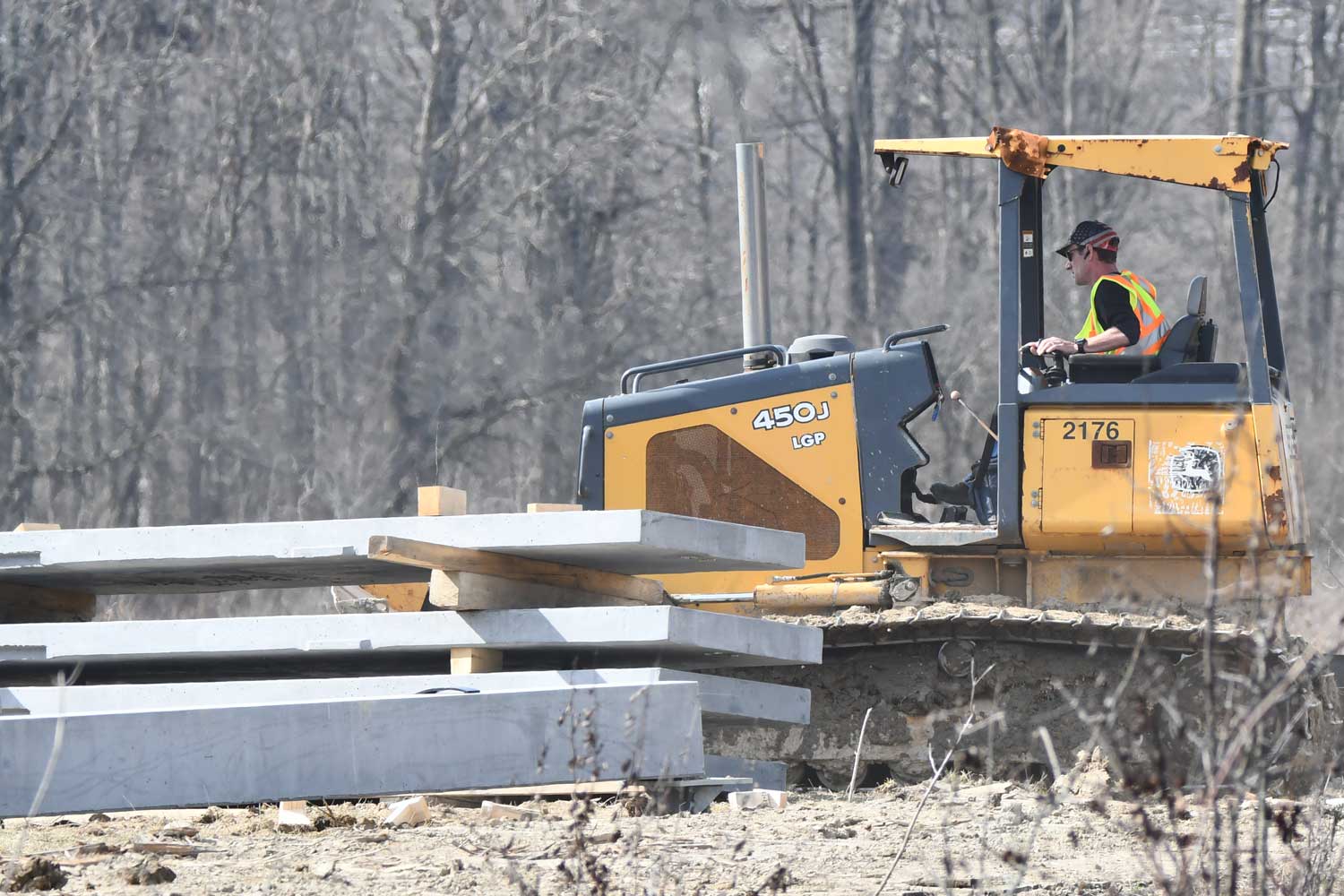 Construction vehicle around construction materials with trees in the background.