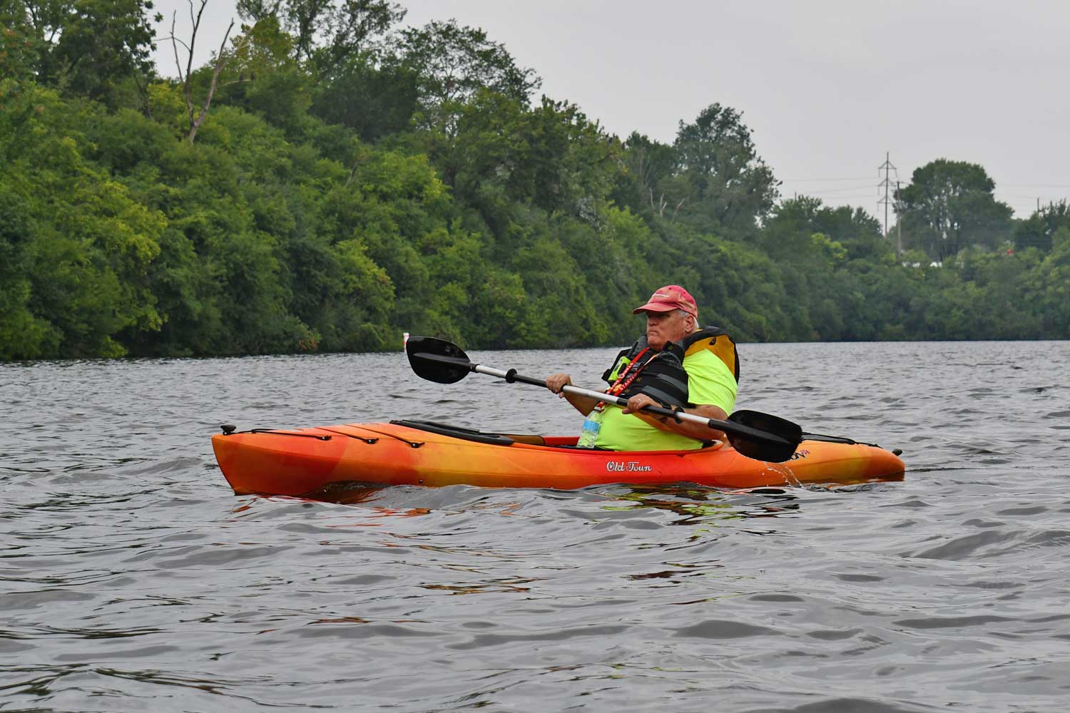 Person in a kayak with water and the tree line in the background.