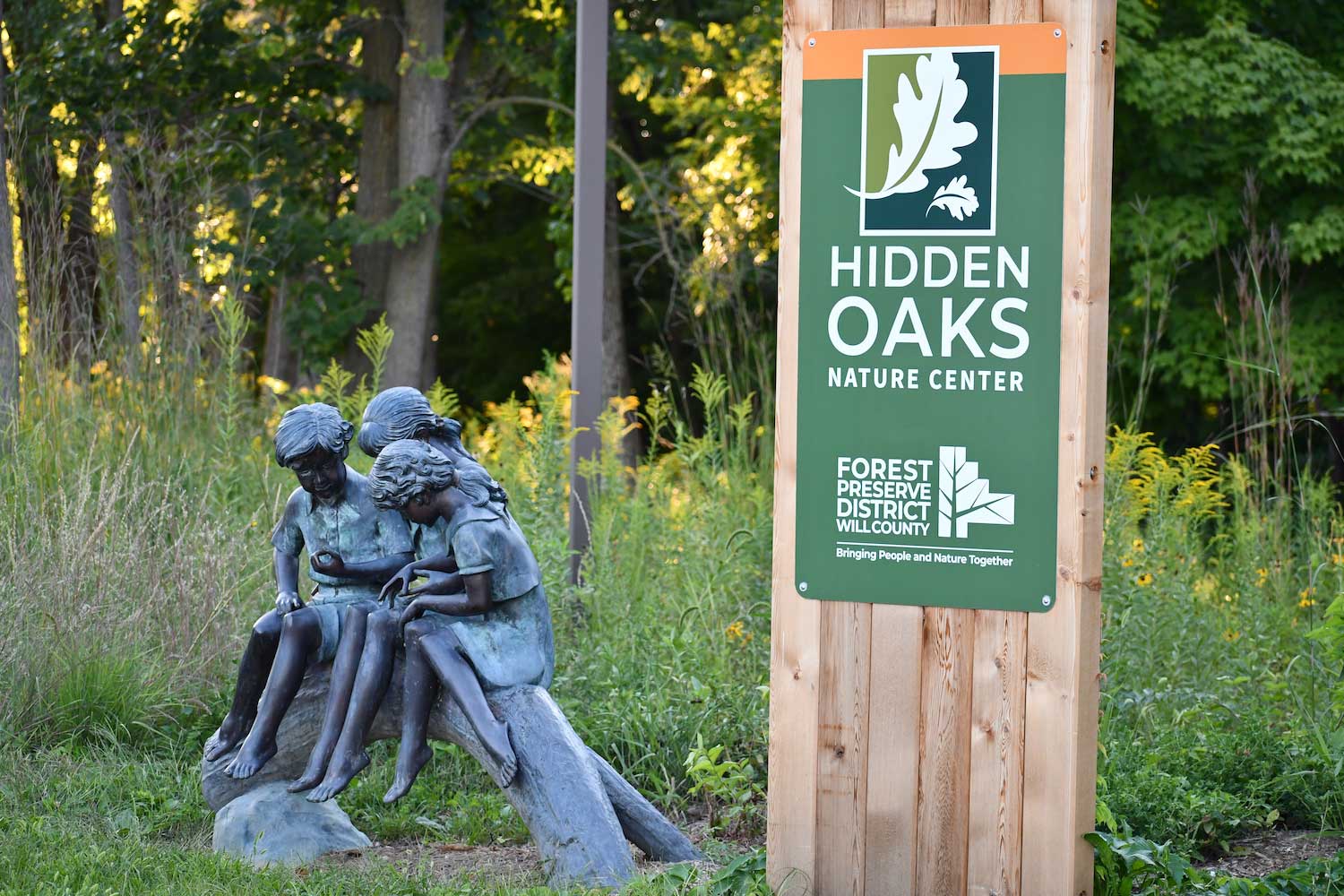 A statue of three children sitting in a log in front of a preserve sign.