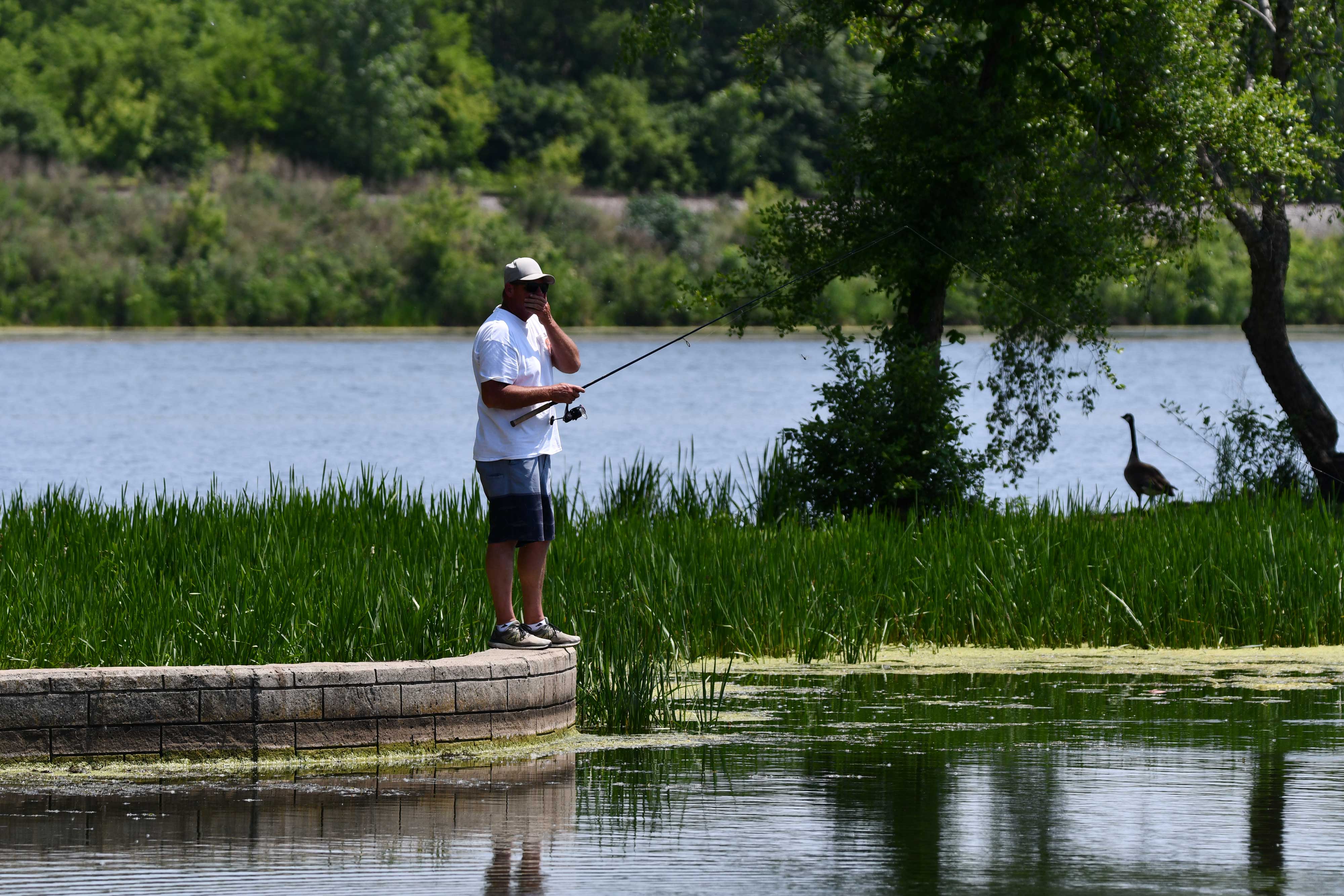 A fisherman along the shore with a fishing pole in his hand.