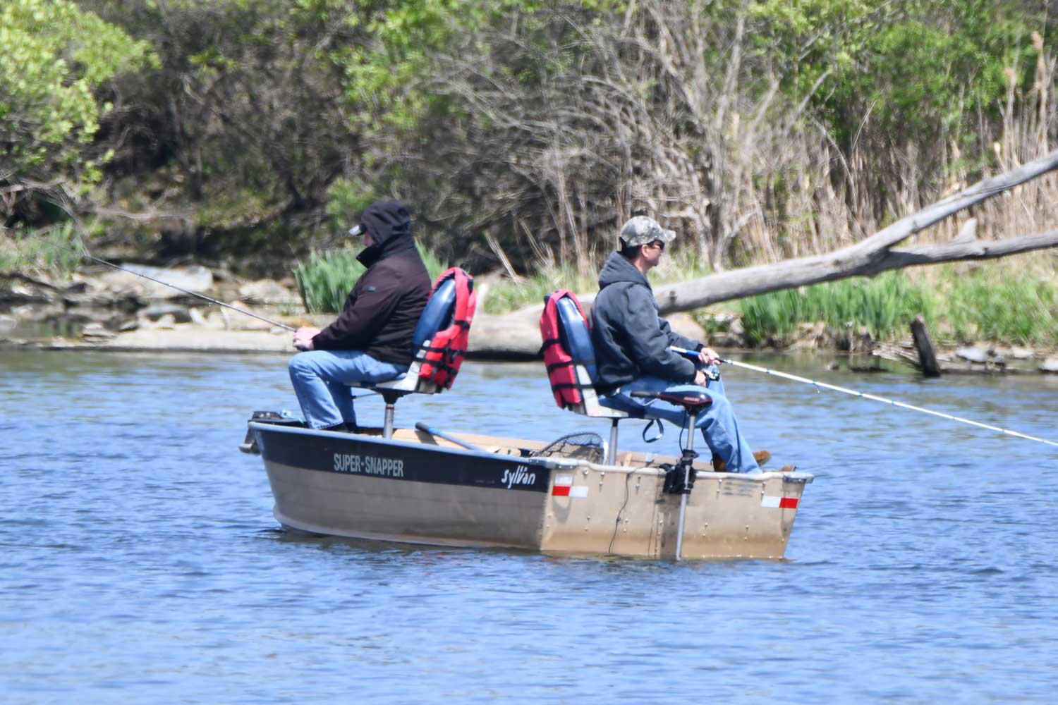 Two people sitting down in a boat while fishing.