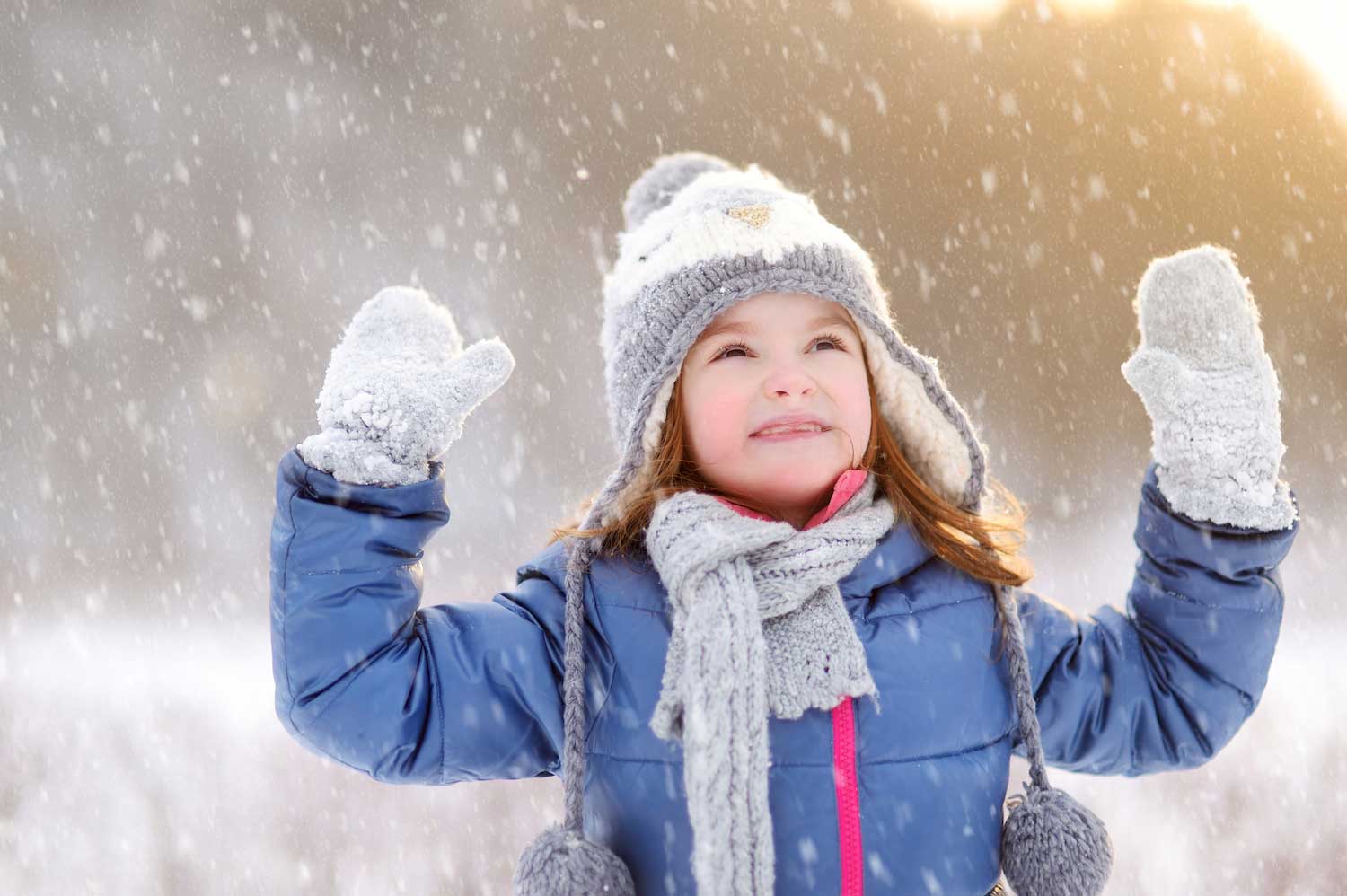 A child dressed for winter looking up at snow falling.