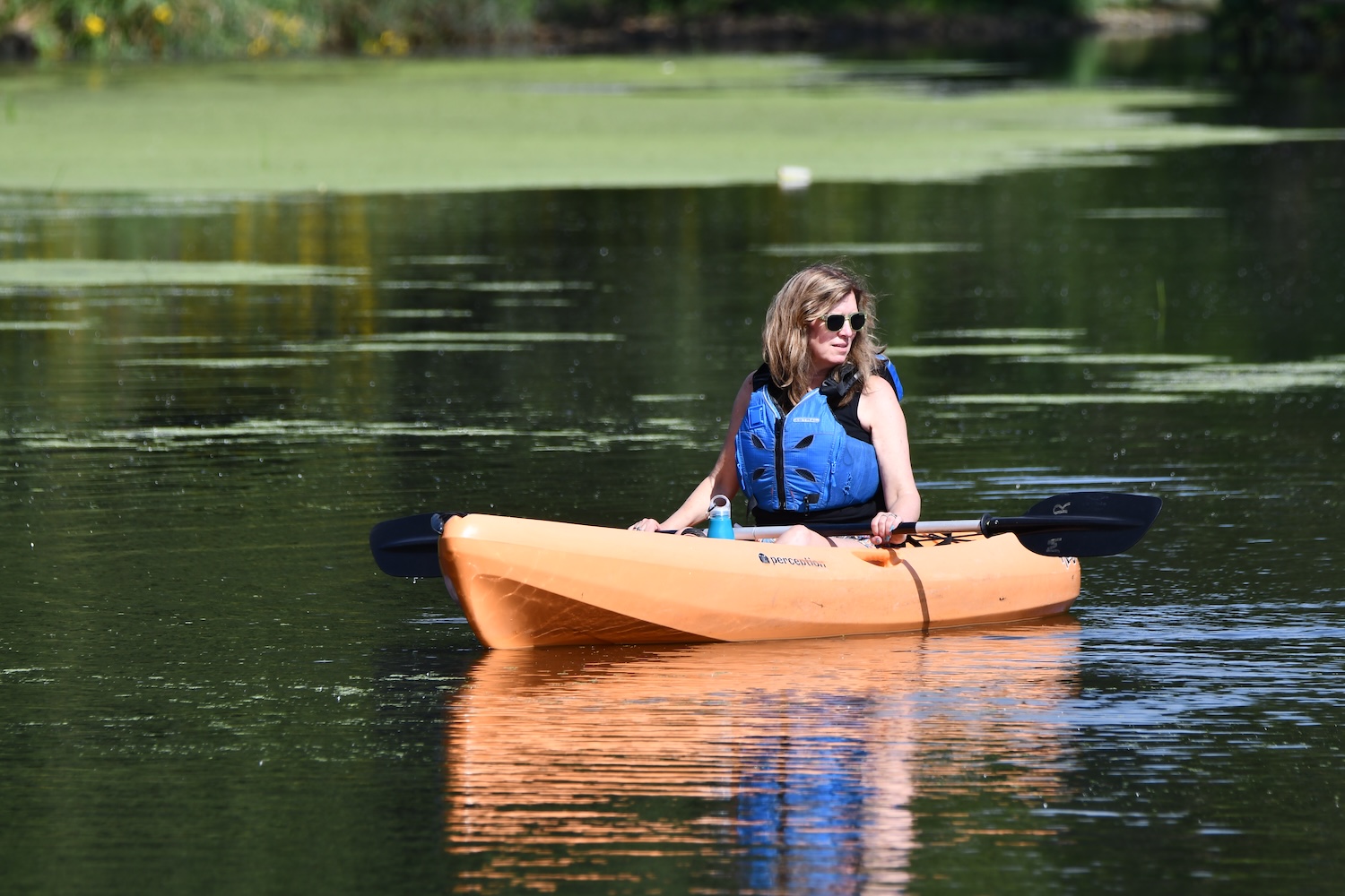 A person wearing a personal flotation device in an orange kayak on the water.