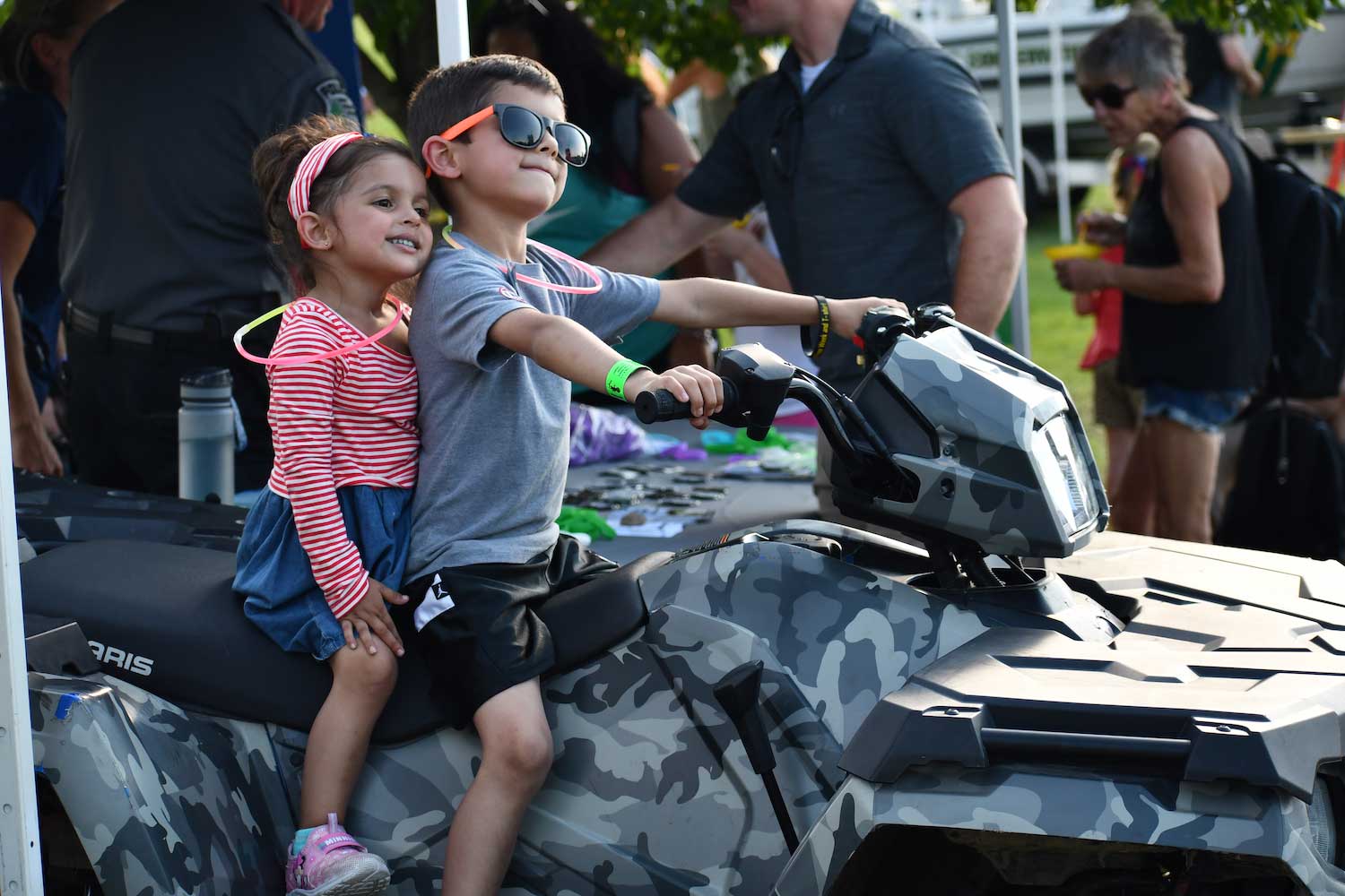 Two young kids sitting on an ATV while posing for a picture.