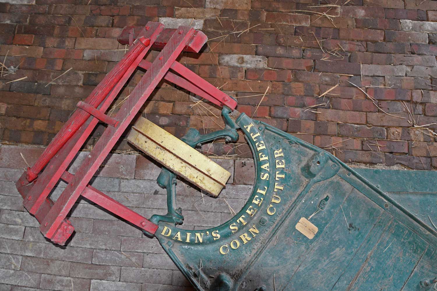 An antique corn cutter on a brick barn floor.