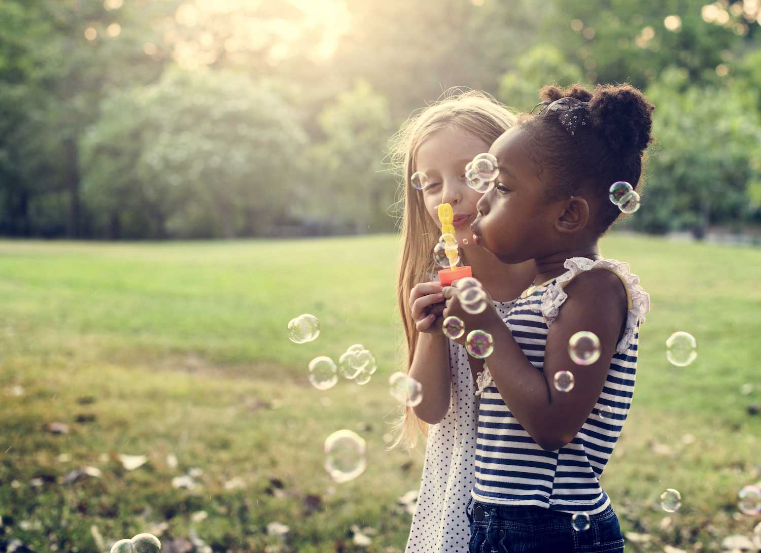 Two girls standing in the grass blowing bubbles.