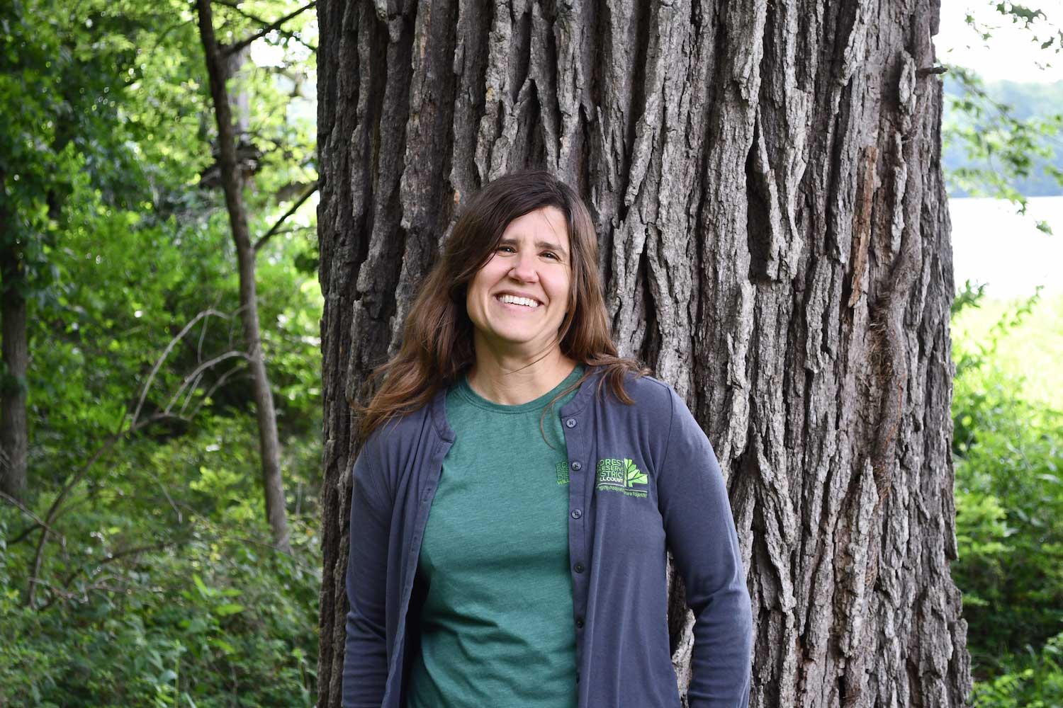 A woman standing in front of a large tree trunk.