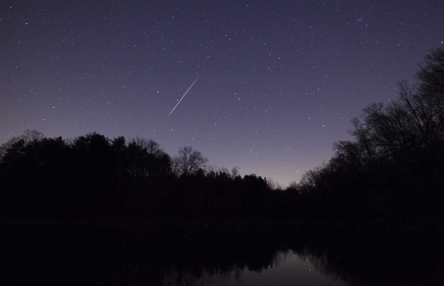 A shooting star falling through the night sky full of stars.