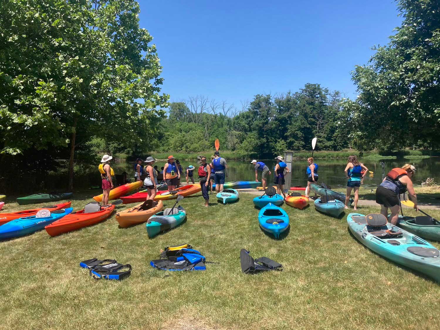 A group of people with kayaks at the water's edge preparing to embark on a kayak trip.