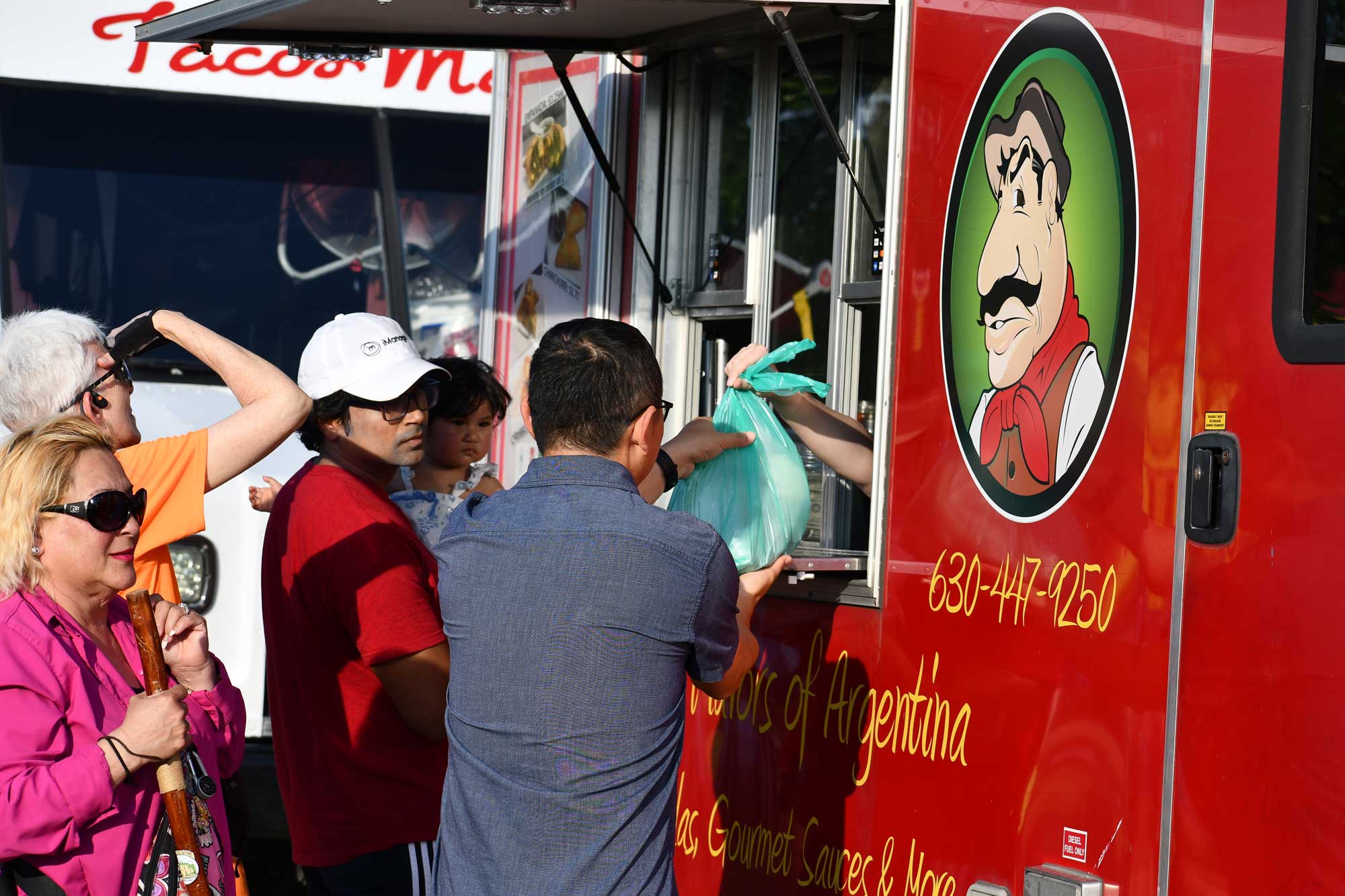 A group of people standing next to a food truck, with a bag of food being passed out of the truck.