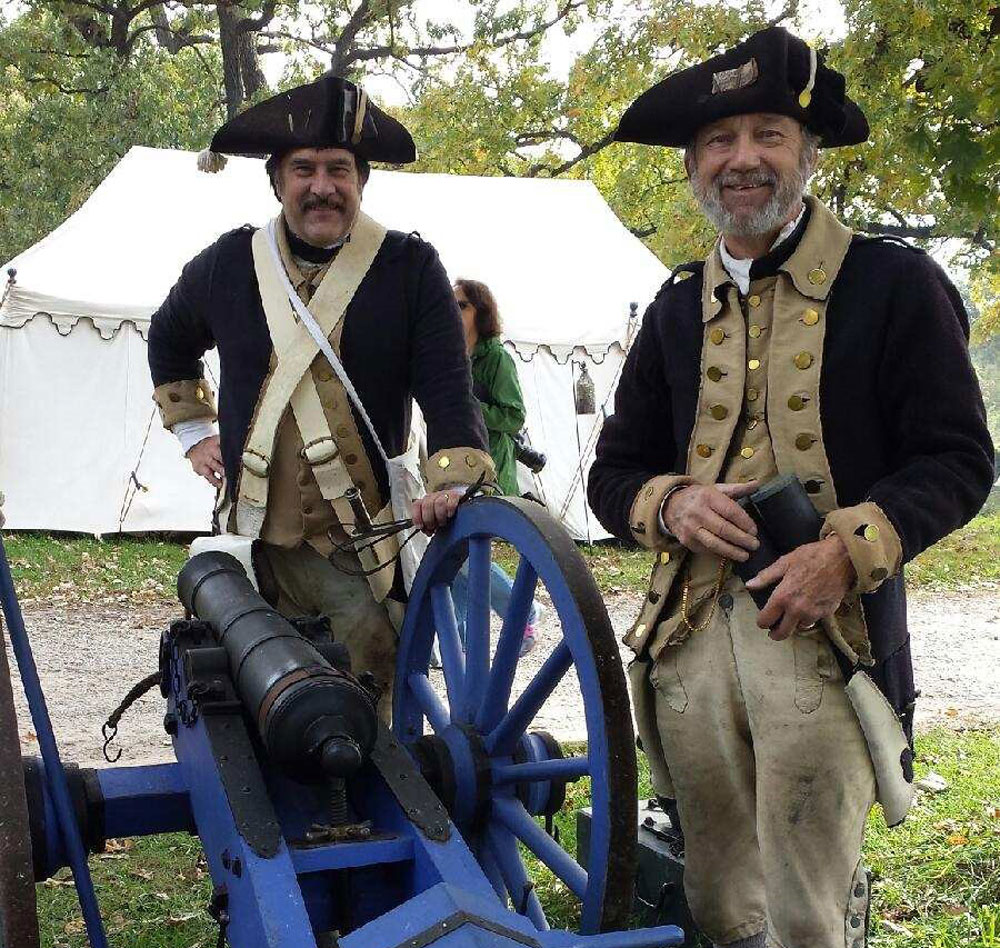 Two people in Civil War-era clothing standing by a cannon.