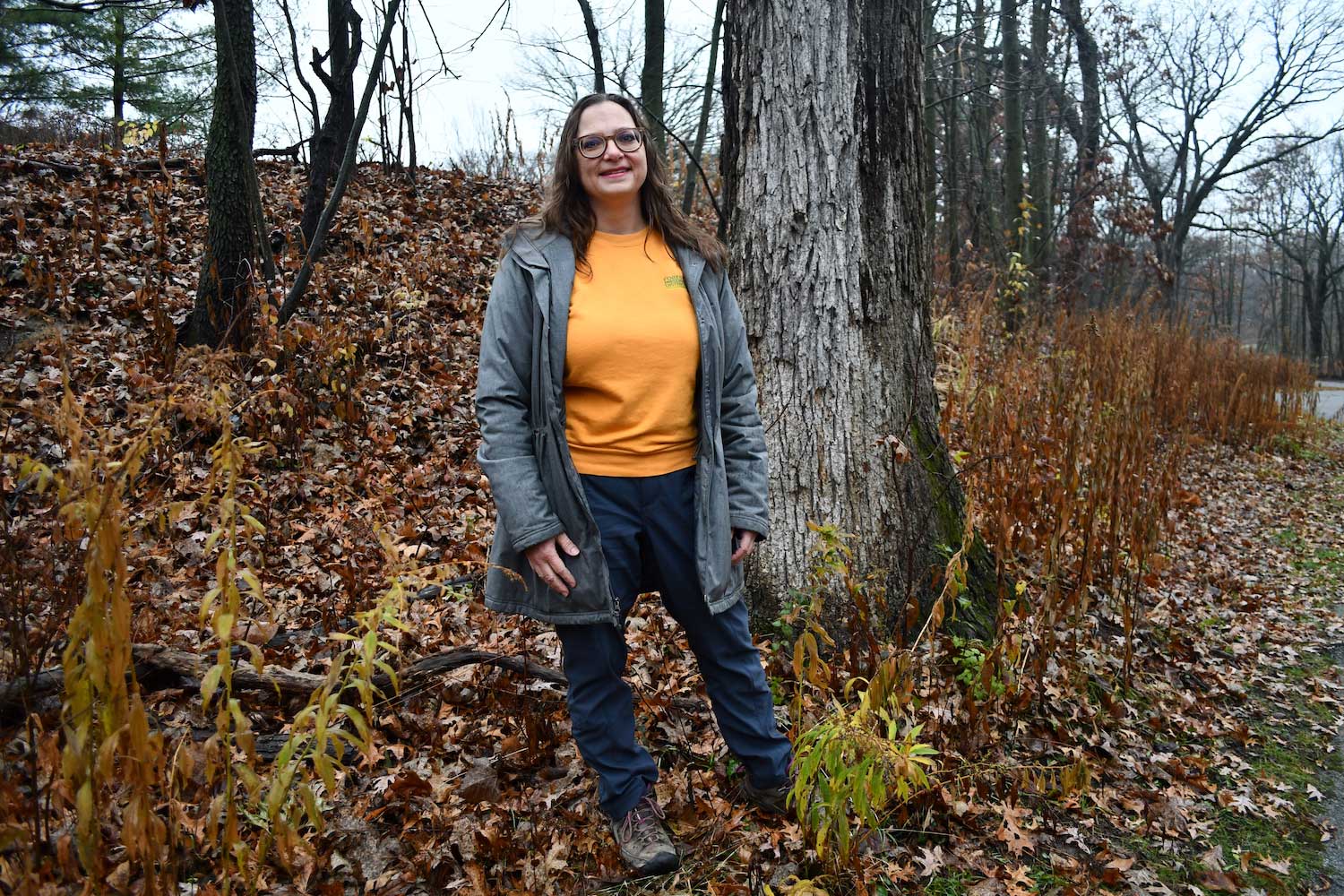 A woman standing in front of a tree along a trail.