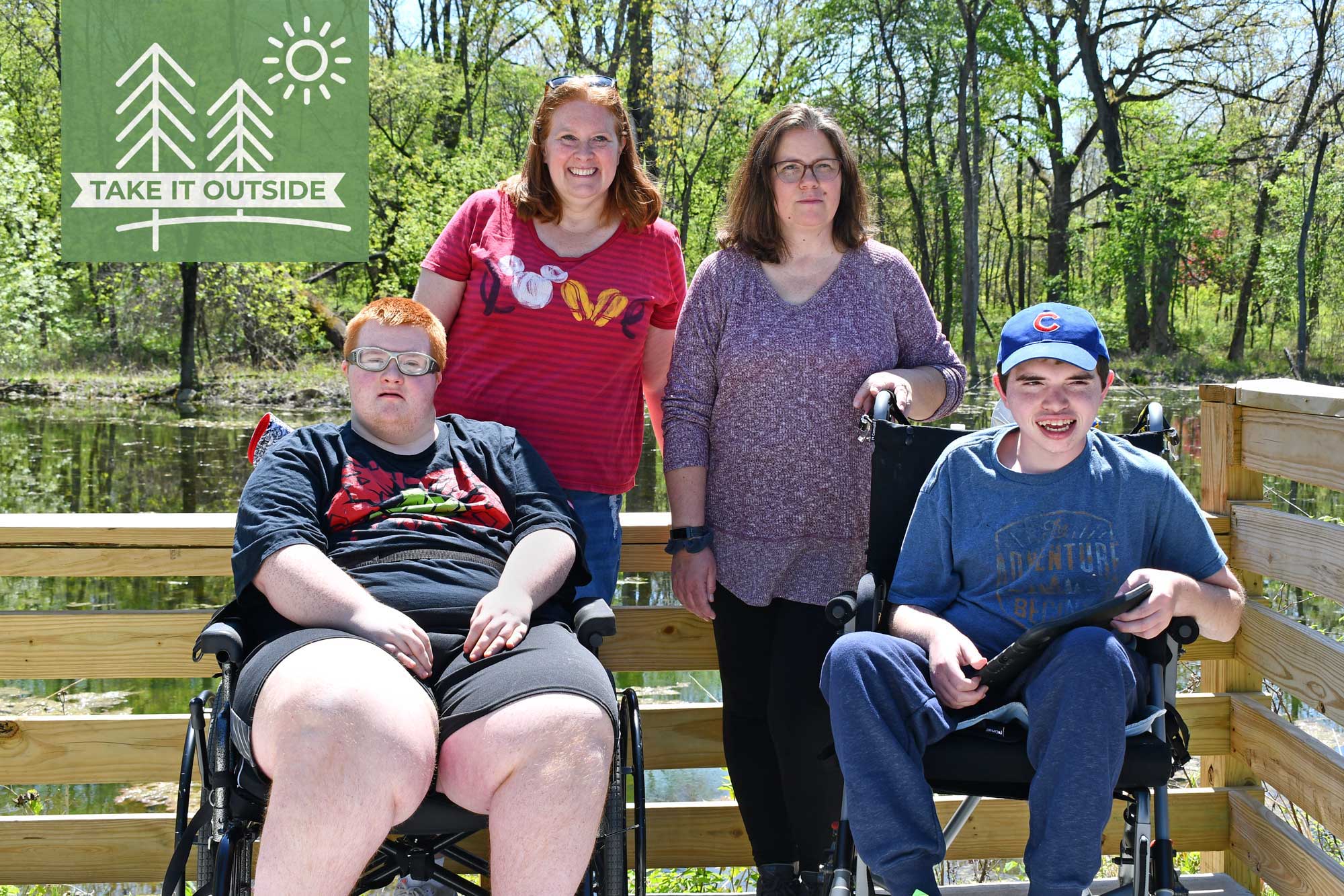 Two women and their sons pose for a photo at a pond overlook.