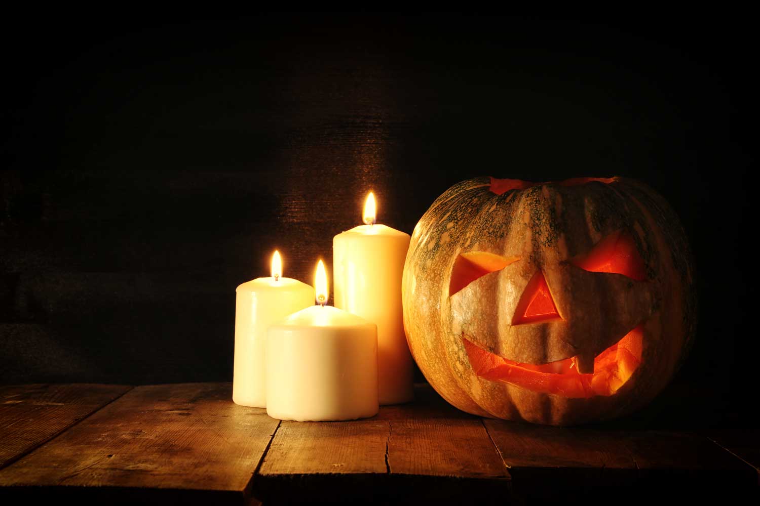 A jack-o'-lantern on a wooden table with three lit candles burning next to it.