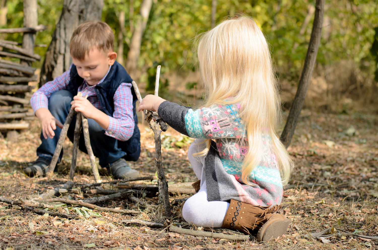 Two children kneeling on the ground playing with sticks.
