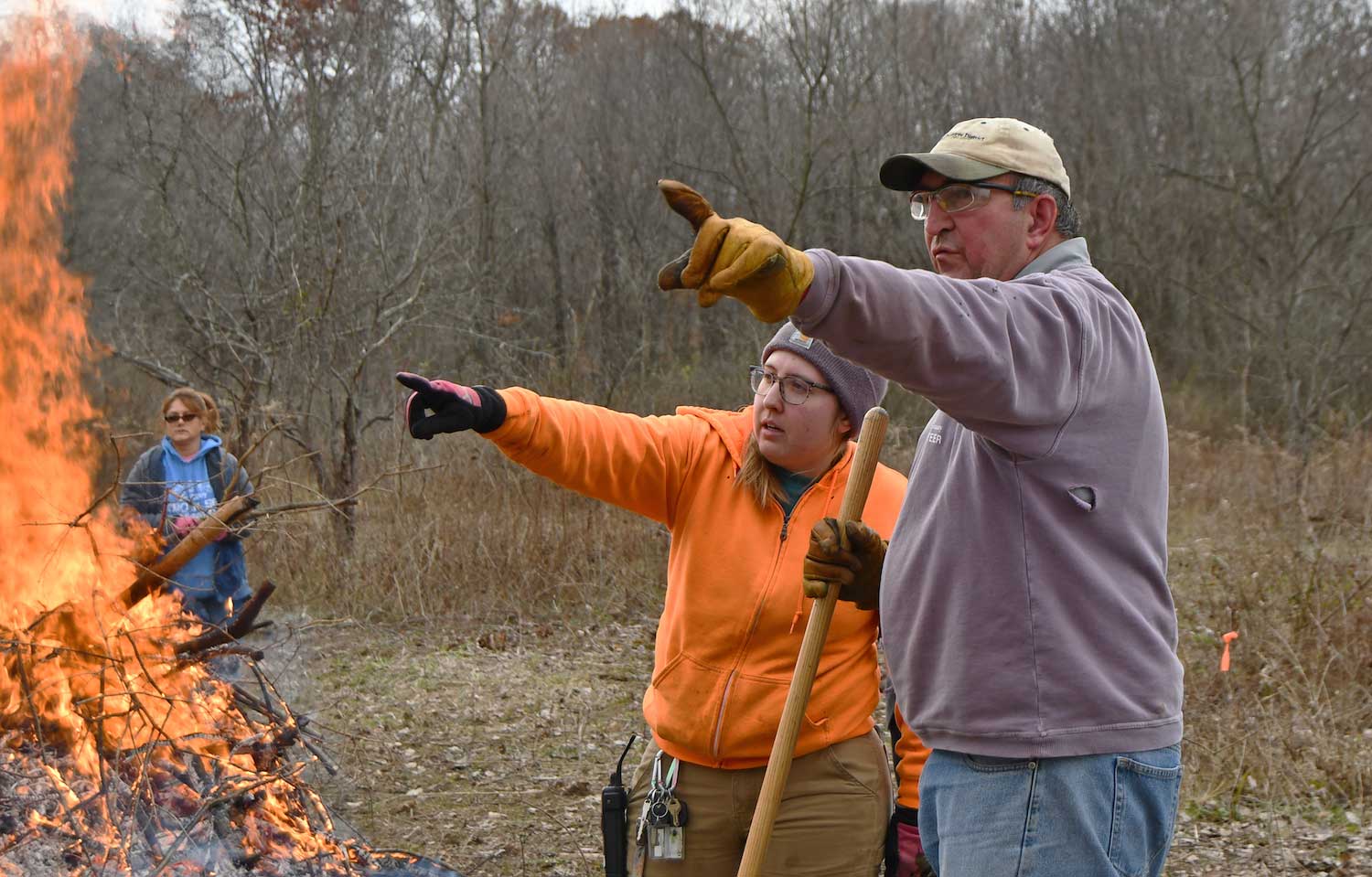 Two people watching over a burning brush pile.