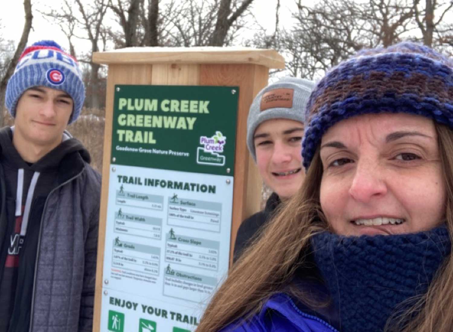 A woman and two sons standing in front of a trailhead sign