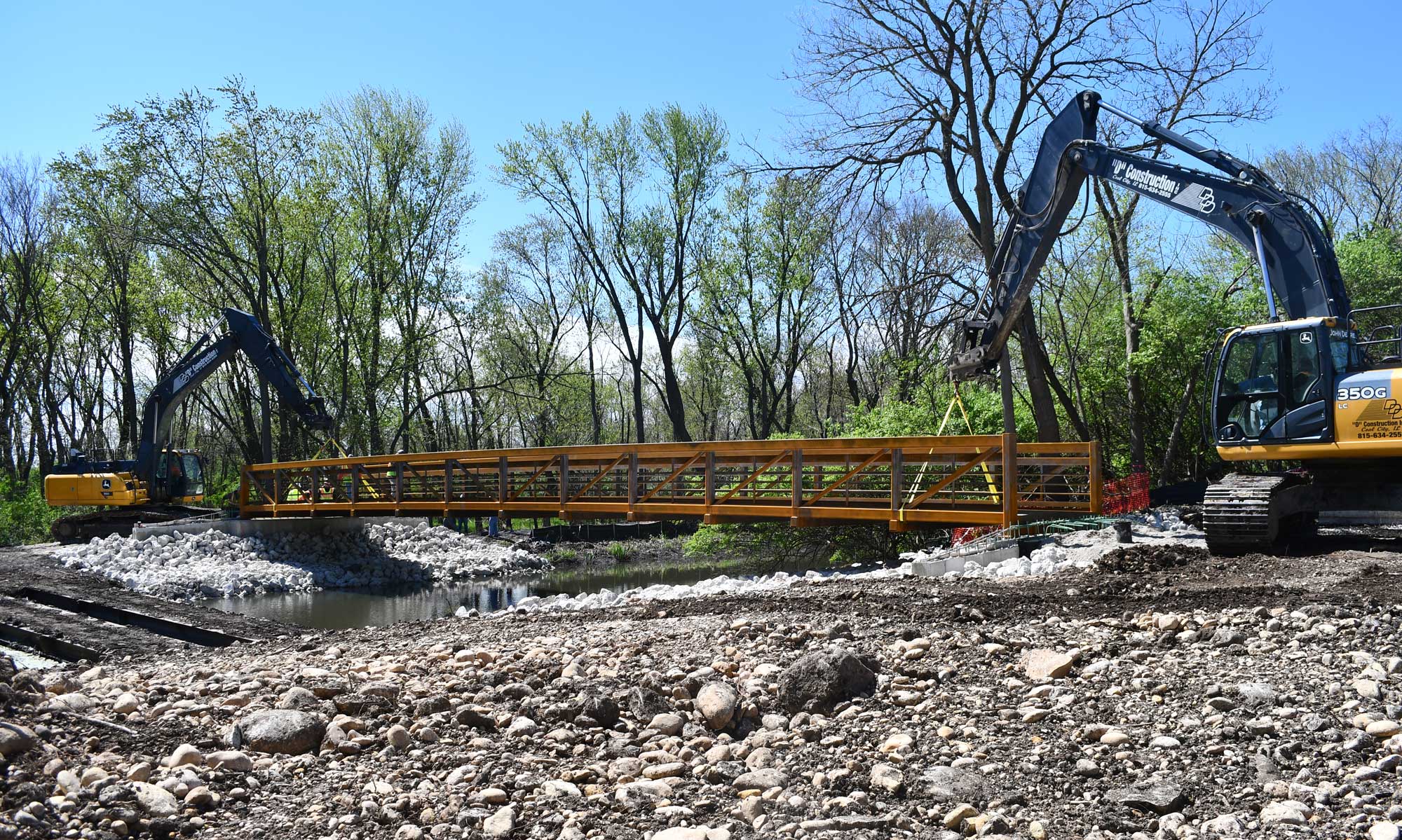 Two excavators set a metal foot bridge in place. 