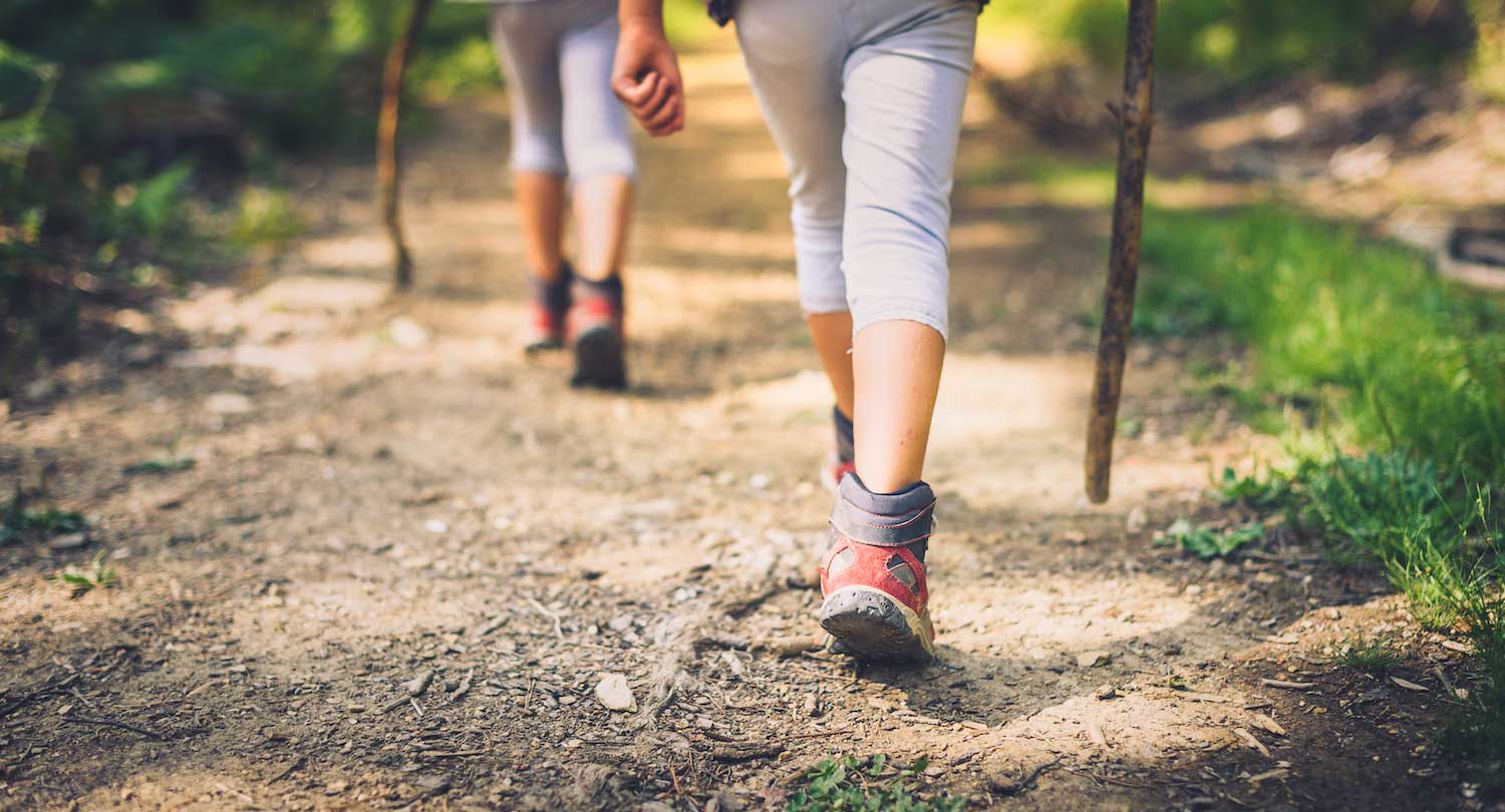 A closeup of the feet of two people hiking on a trail with walking sticks.