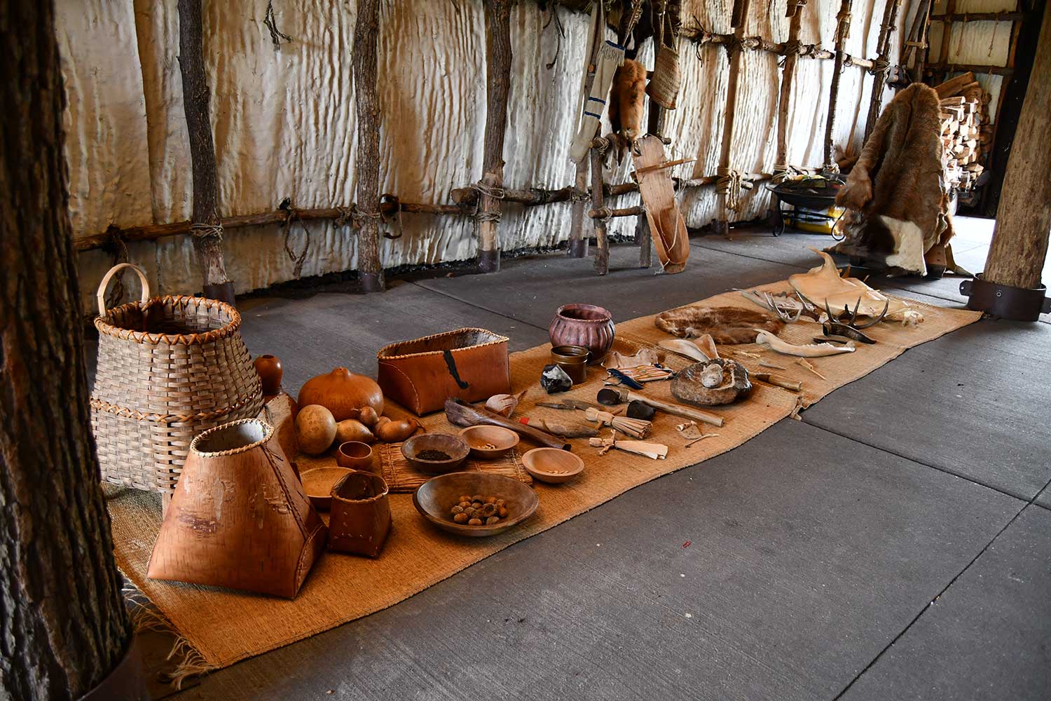 A collection of replica baskets, tools and other items using by Native peoples on the ground inside a longhouse.