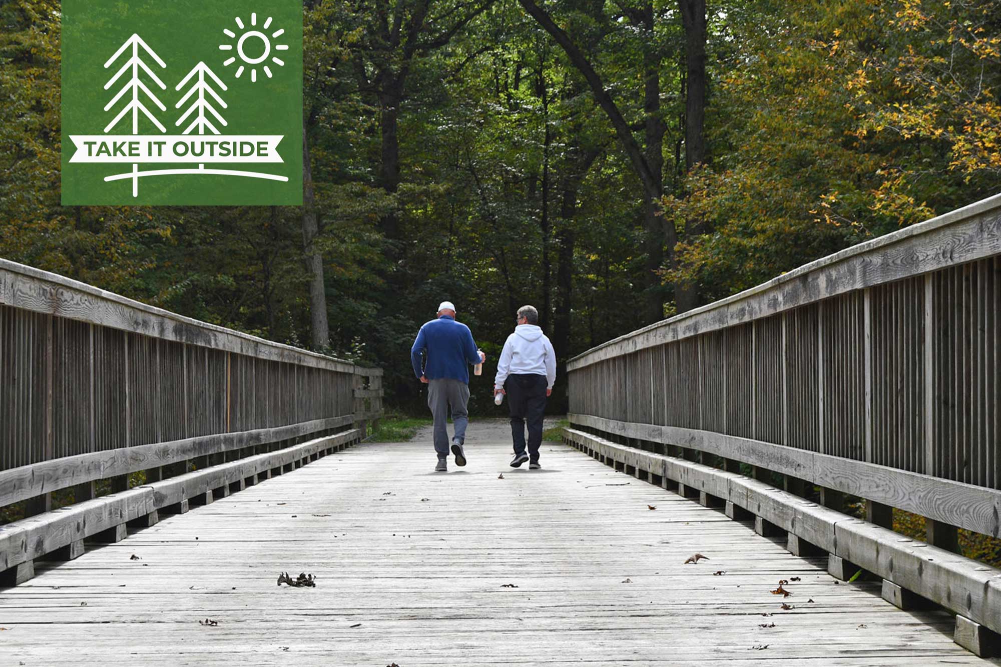 A man and woman walking across a trail bridge.