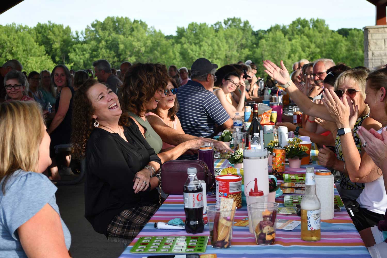 A picnic shelter pull of people sitting at picnic tables playing bingo.