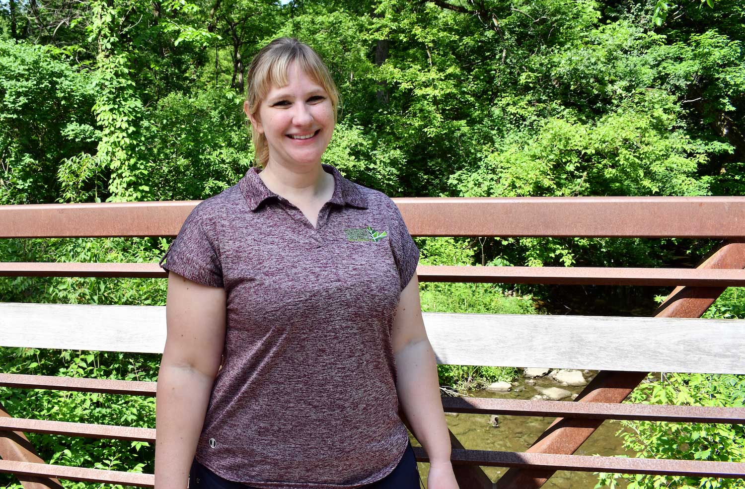 A person standing on a metal bridge with trees in the background.