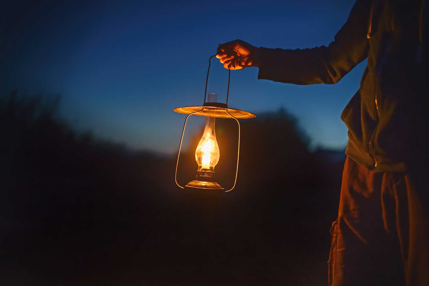 A person holding a lantern outside in the dark.