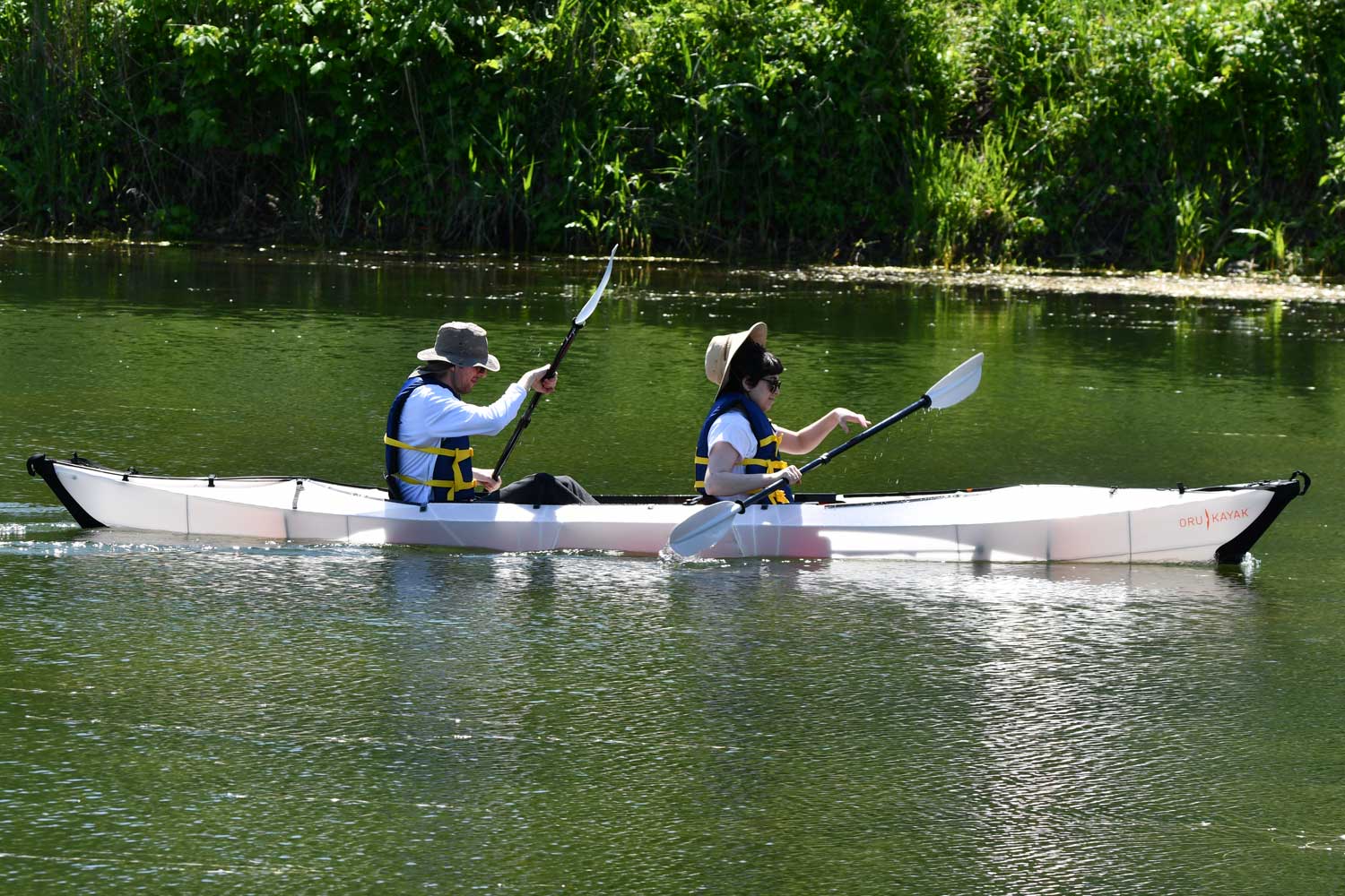 Two people in a canoe with water and tree line in the background.