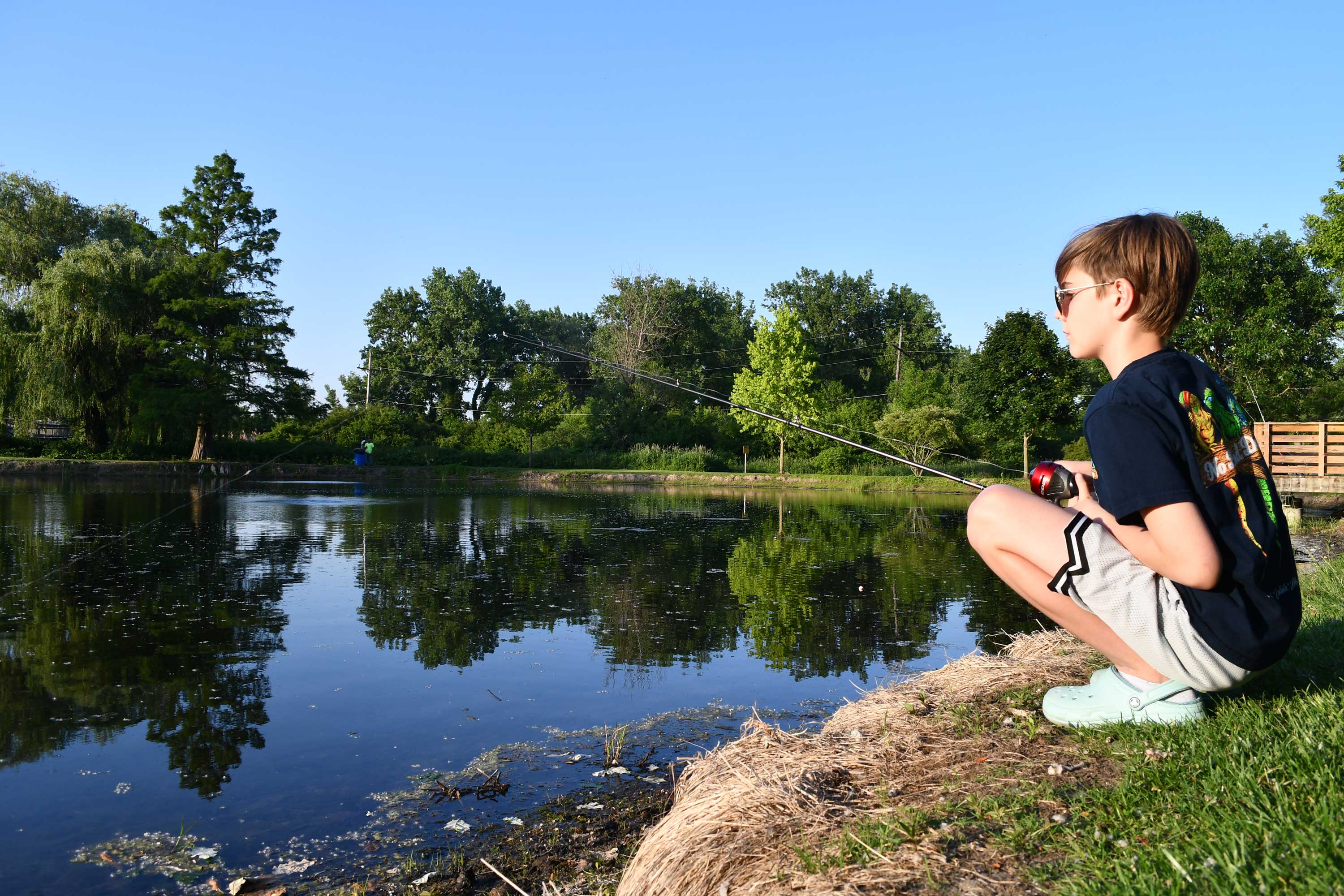 A child fishes along the shore of a lake.