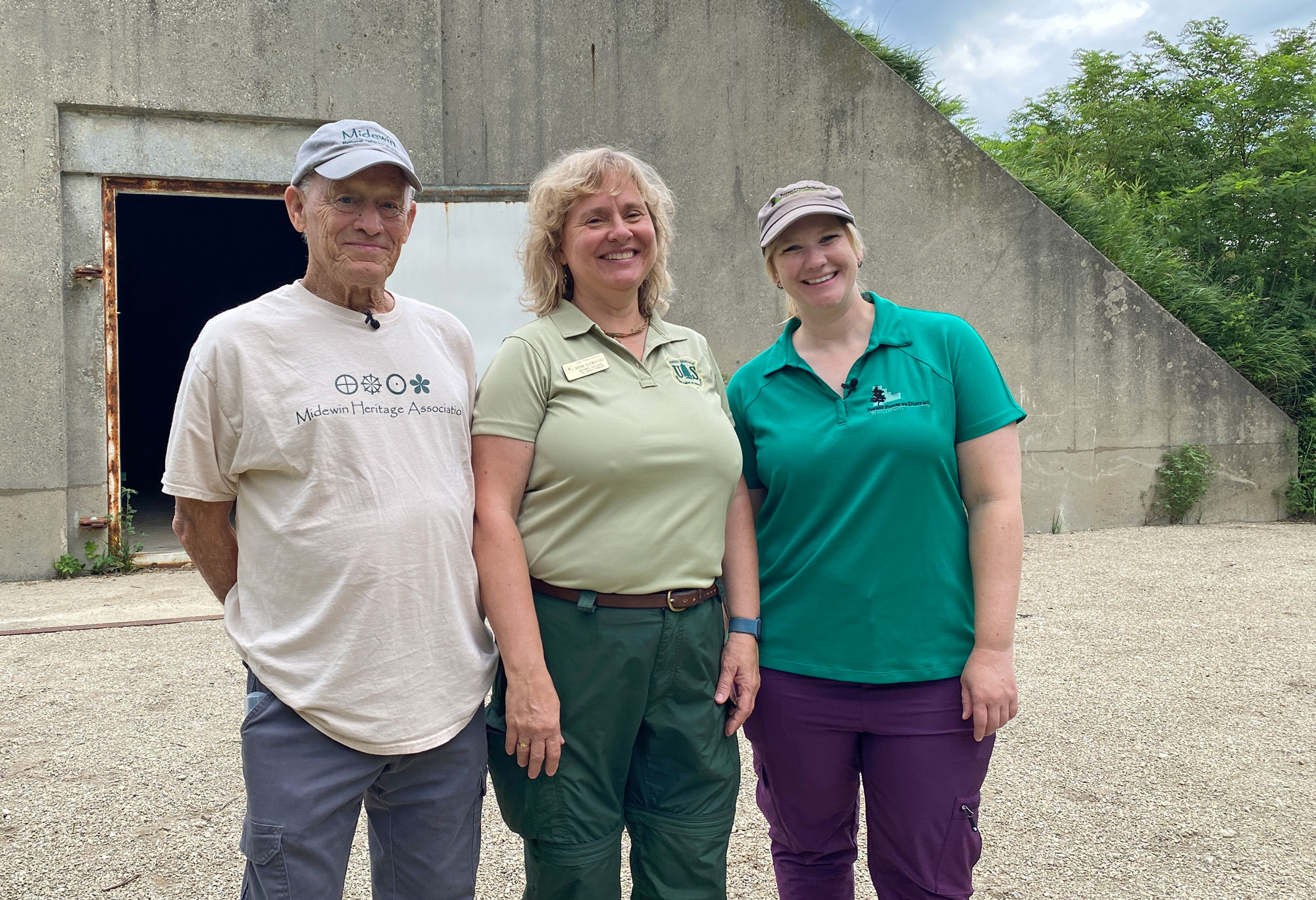 Three people stand in front of an old ammunition bunker.